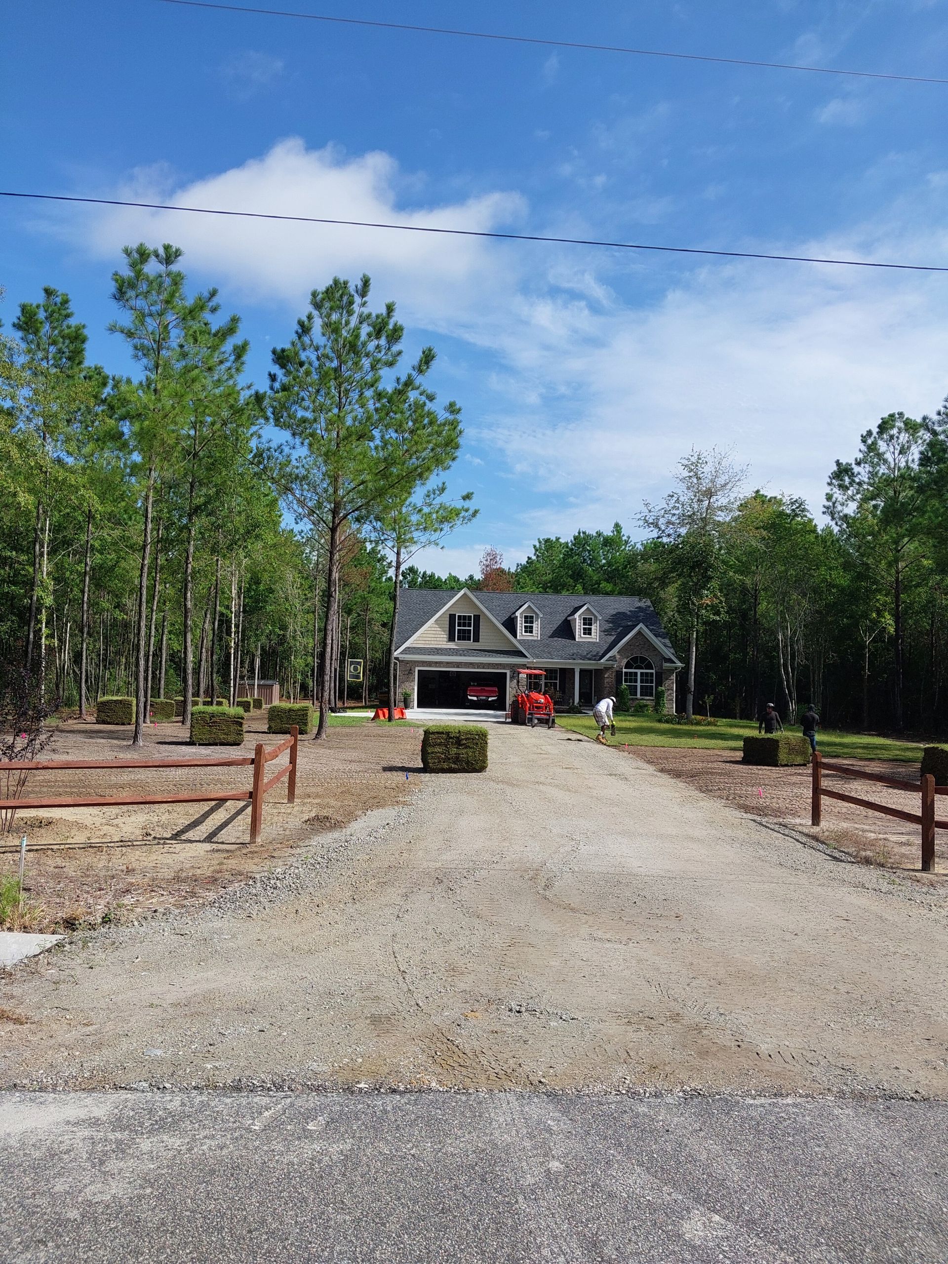 A gravel driveway leads to a house with a garage, a tractor, and trees on a sunny day.
