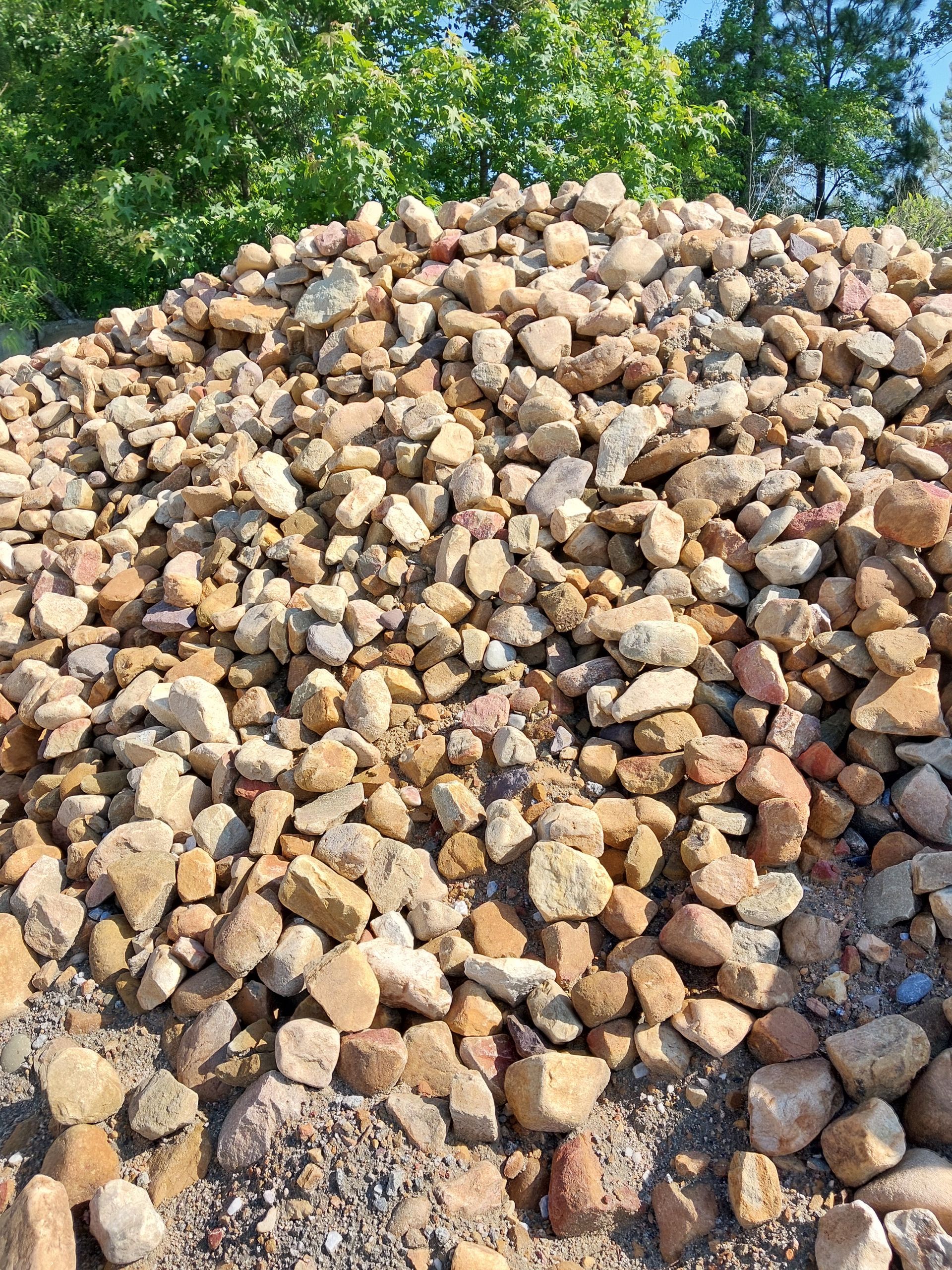 Pile of tan and brown rocks outdoors with green trees in the background.