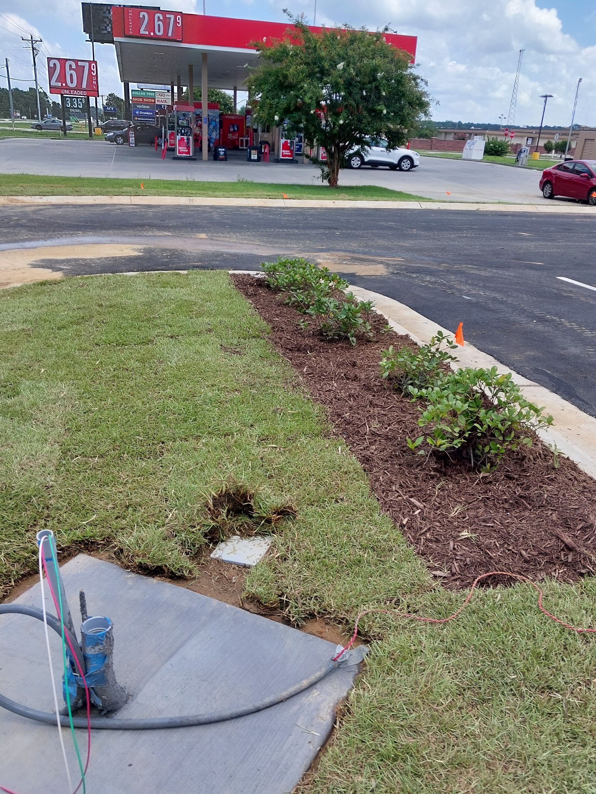 Landscaped area in front of a gas station. Freshly laid sod and mulch beds with bushes border the parking area.