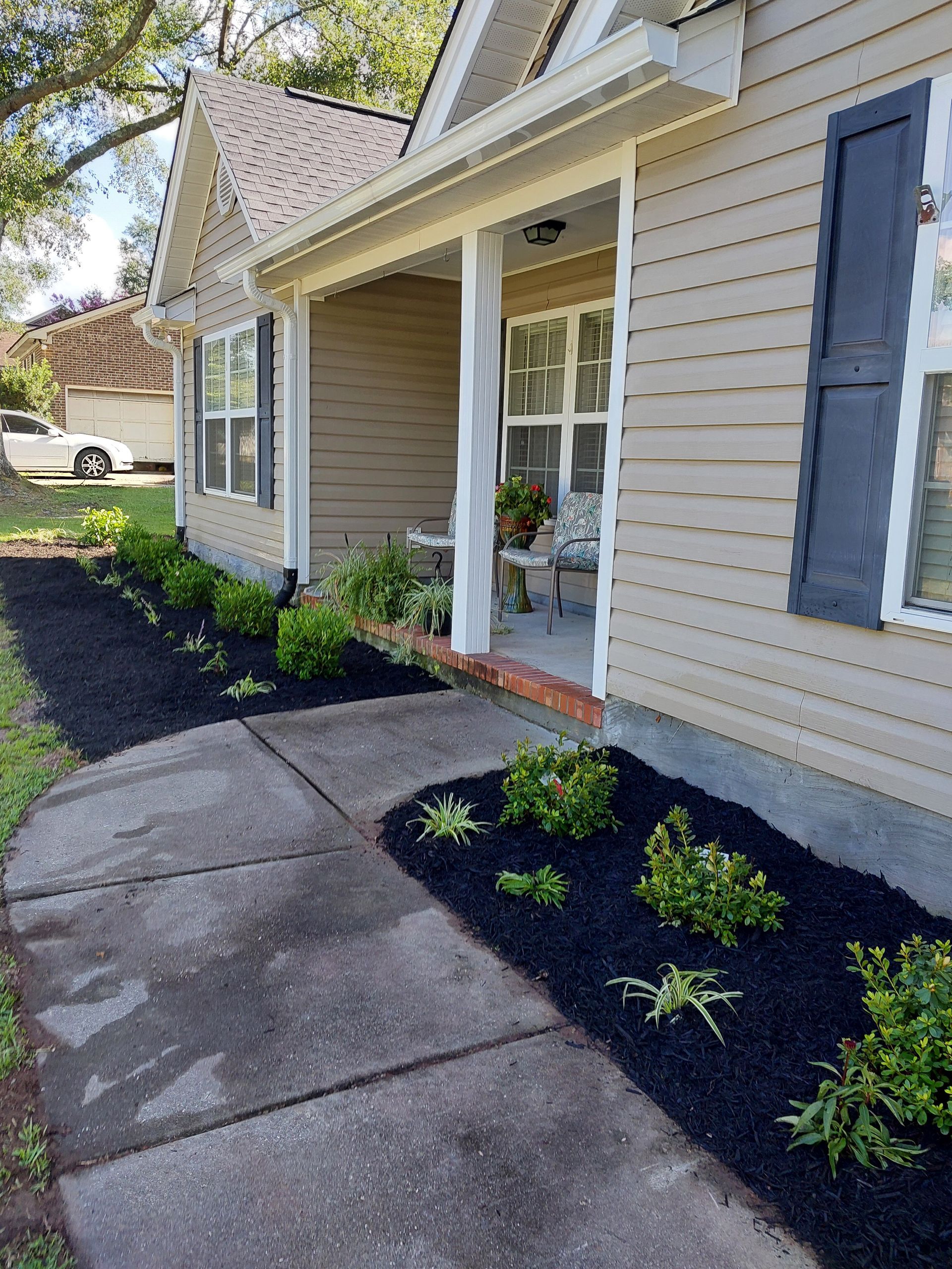 Tan house with black mulch landscaping. Dark gray sidewalk leads to the front door. Green plants are visible in the mulch beds.