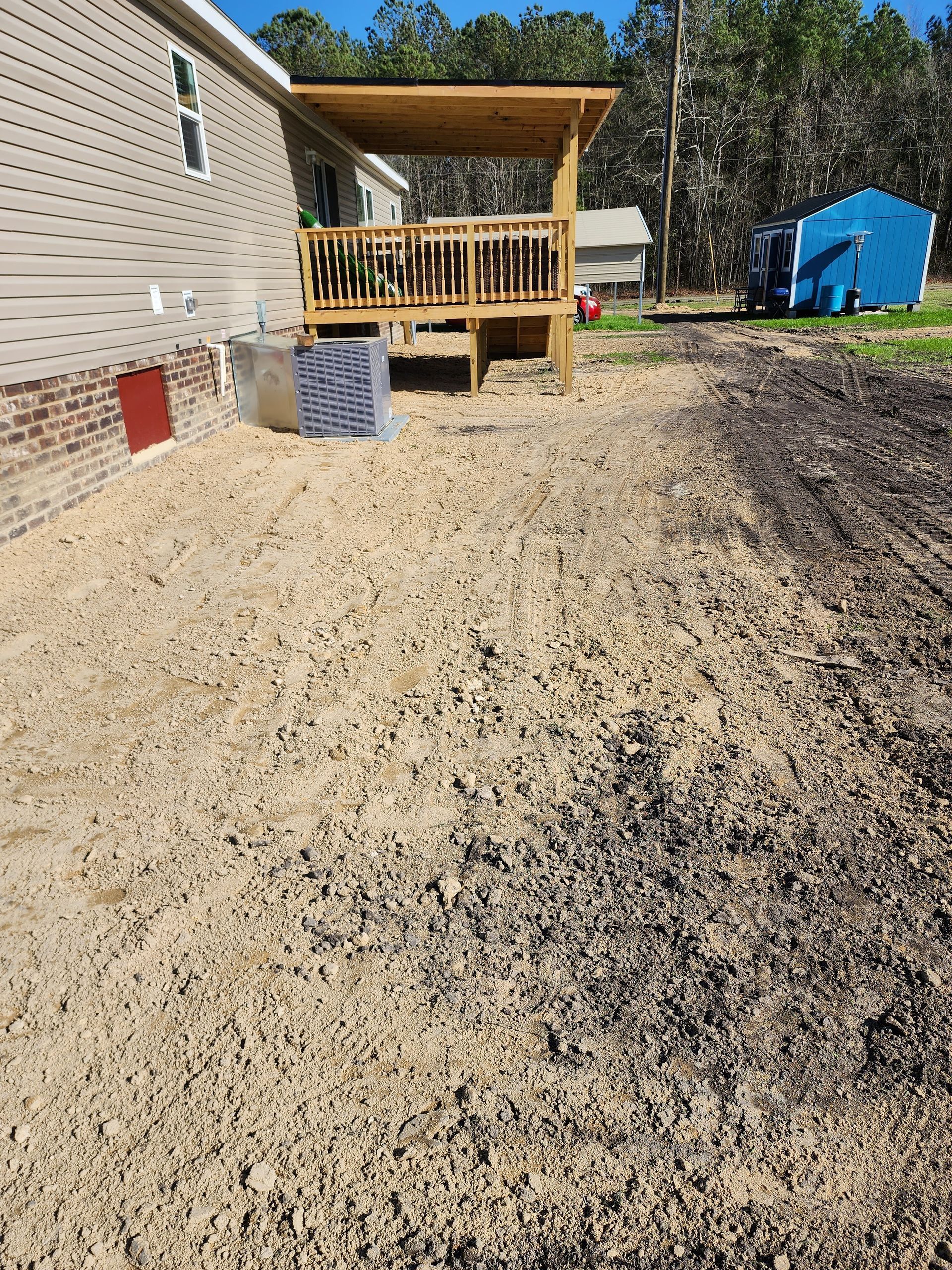 A gravel-covered yard leads to a wooden deck attached to a light-colored house. A blue shed is in the background.