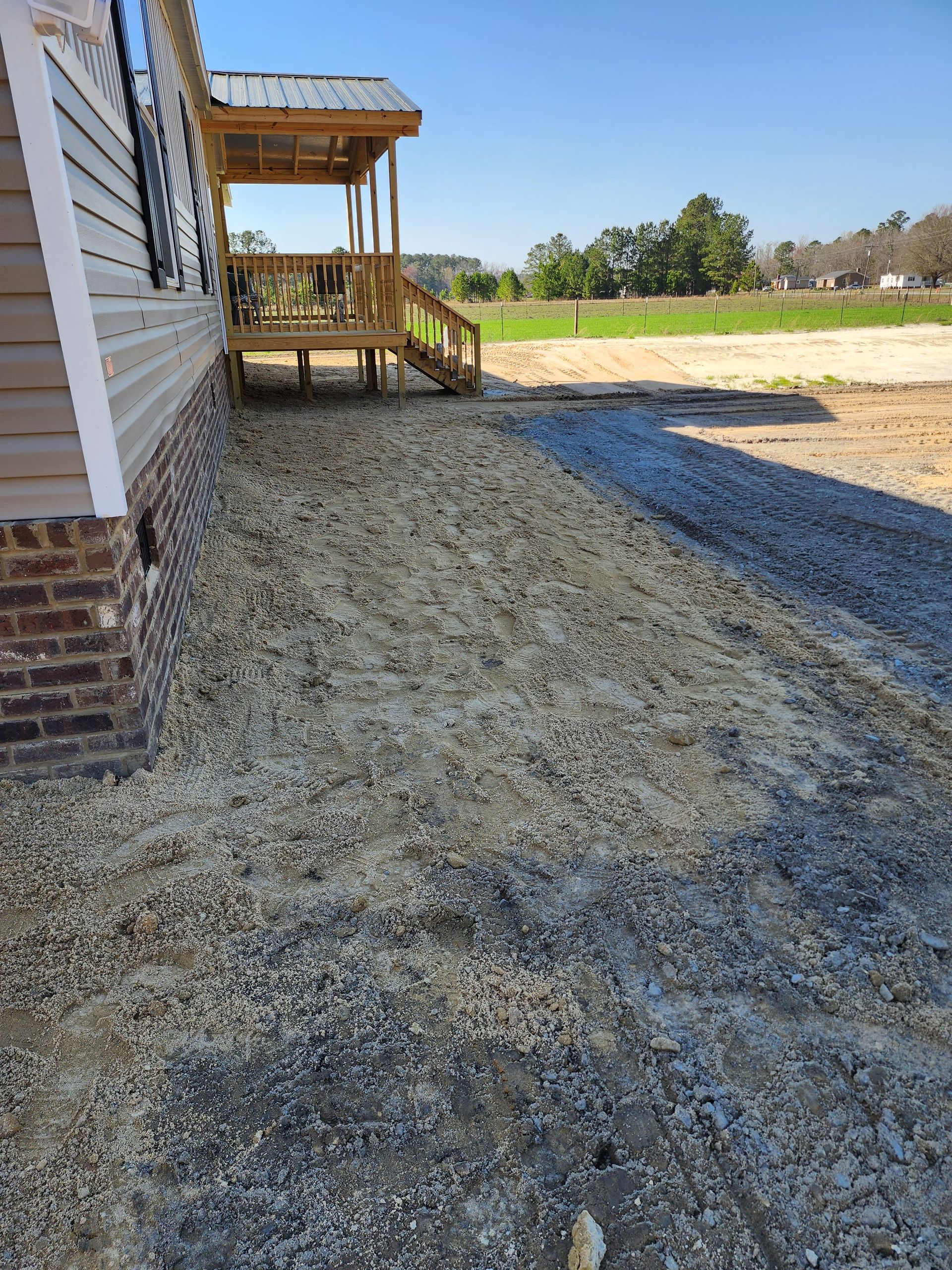 A house with a gravel walkway alongside it, leading to a wooden porch under a blue sky.