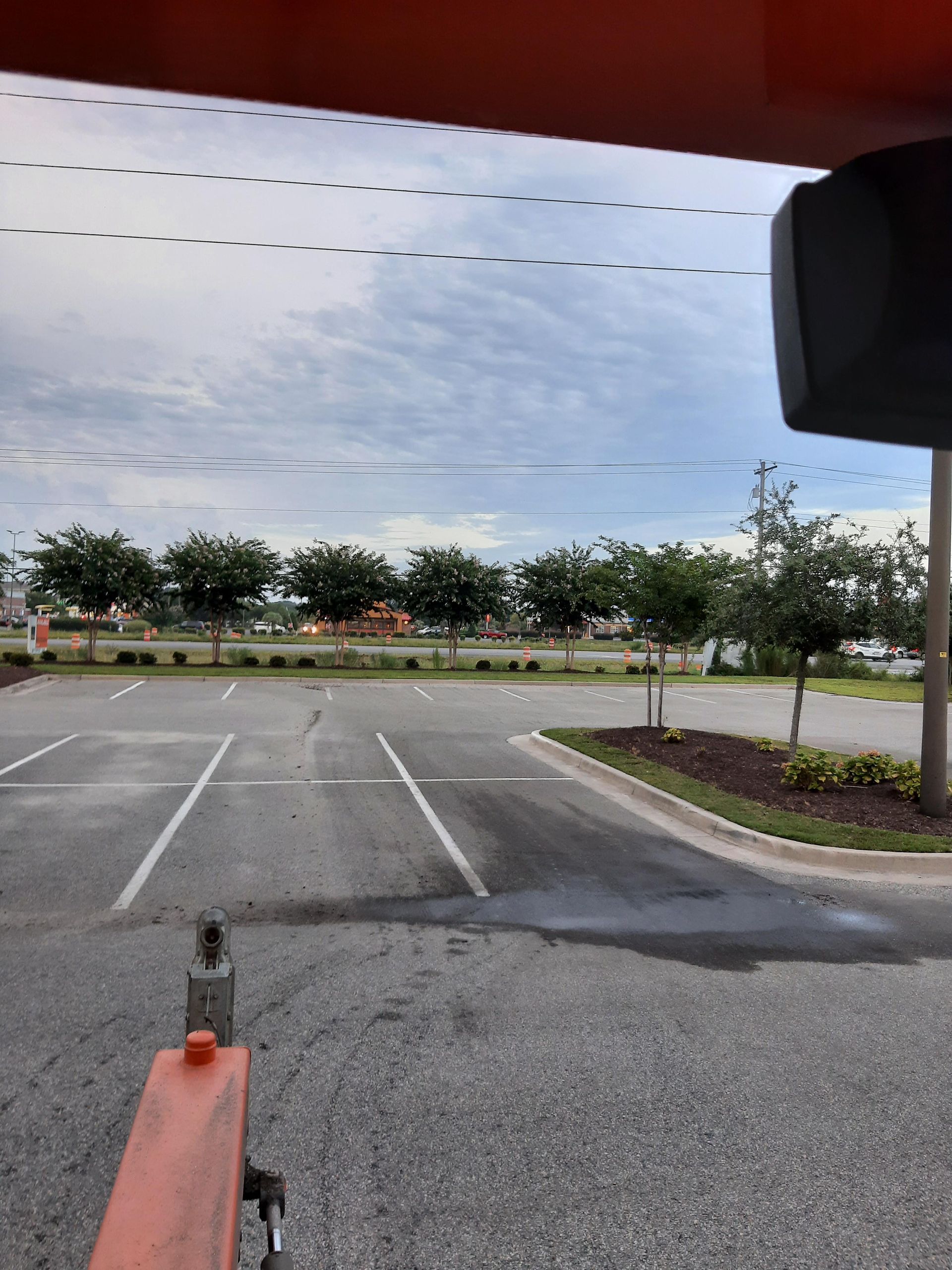 View from inside a vehicle overlooking a parking lot with empty spaces, trees, and a cloudy sky.