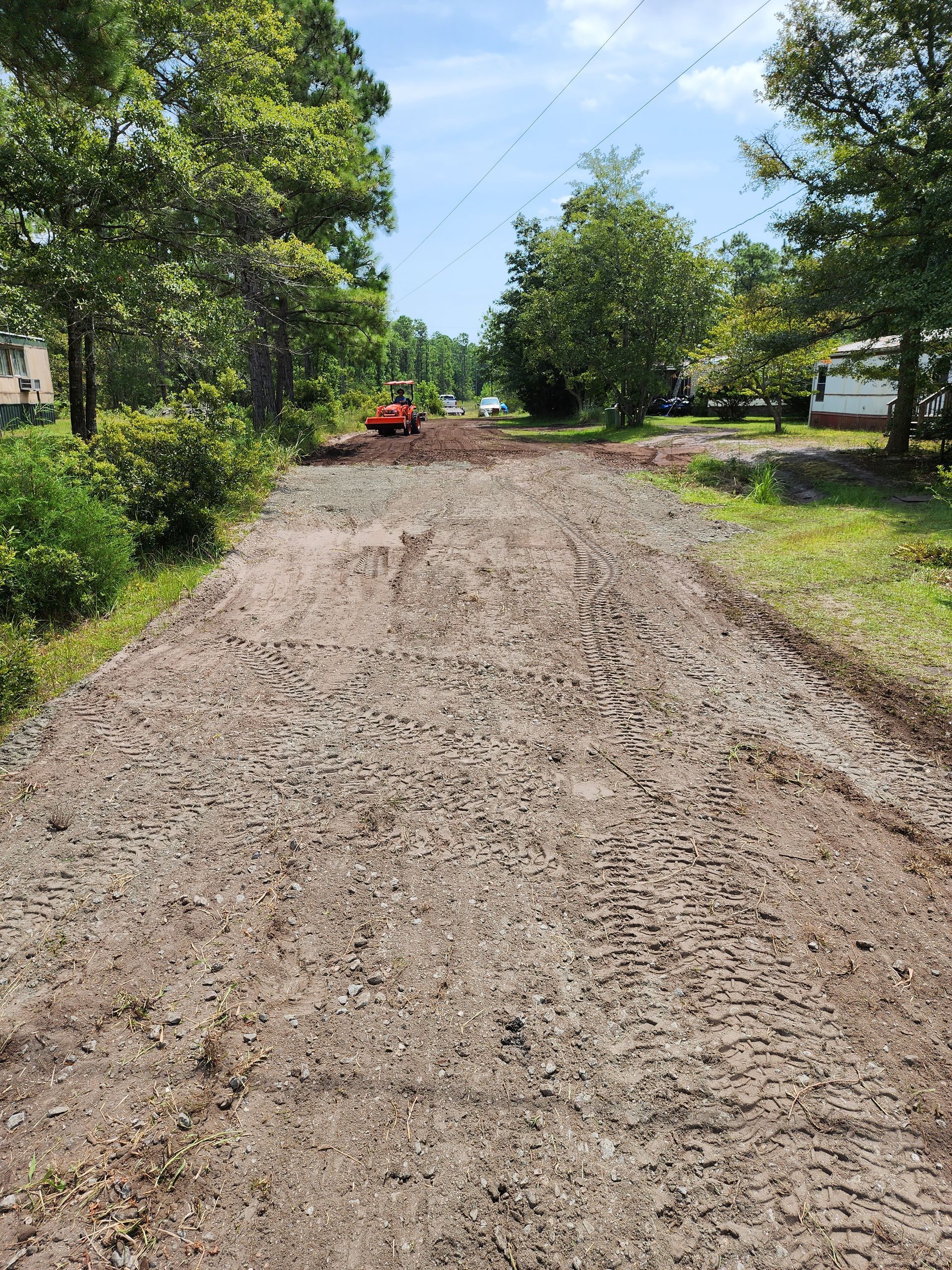 Gravel road with tire tracks, trees on either side, and an orange construction vehicle in the distance.