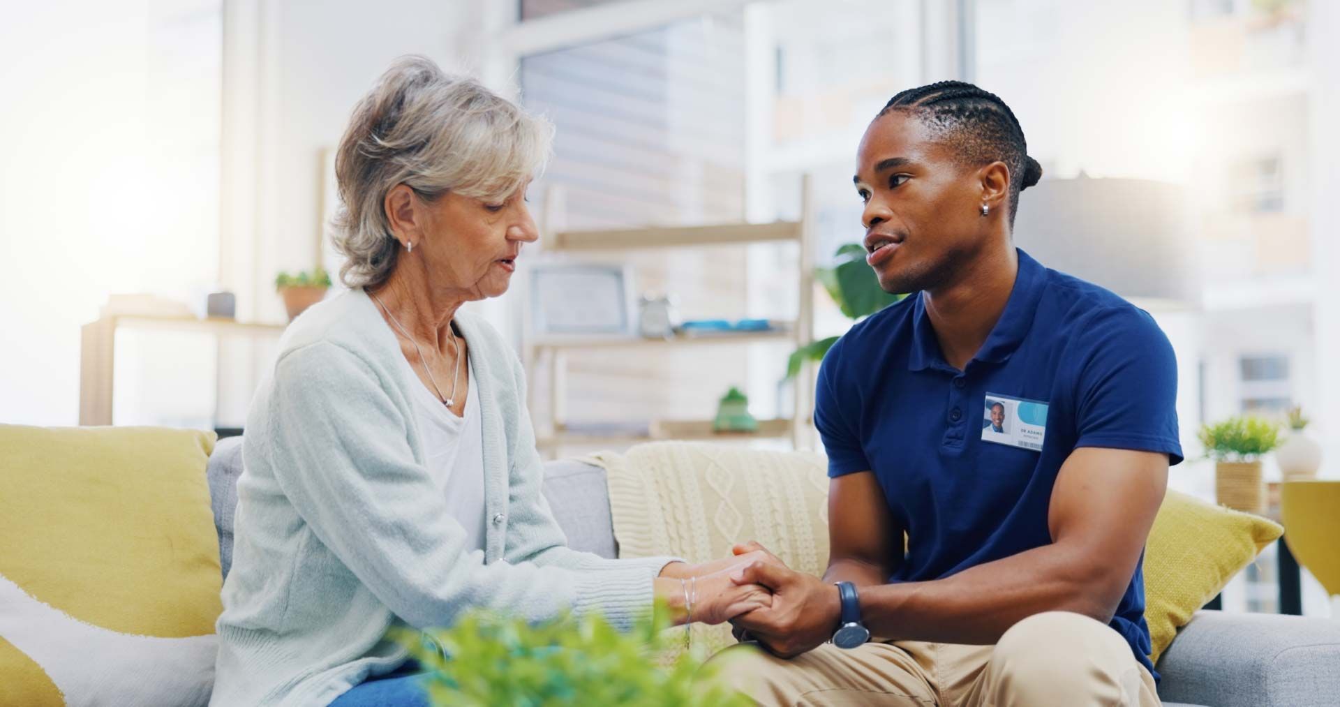 Woman holding hands with older person on a couch, offering support.
