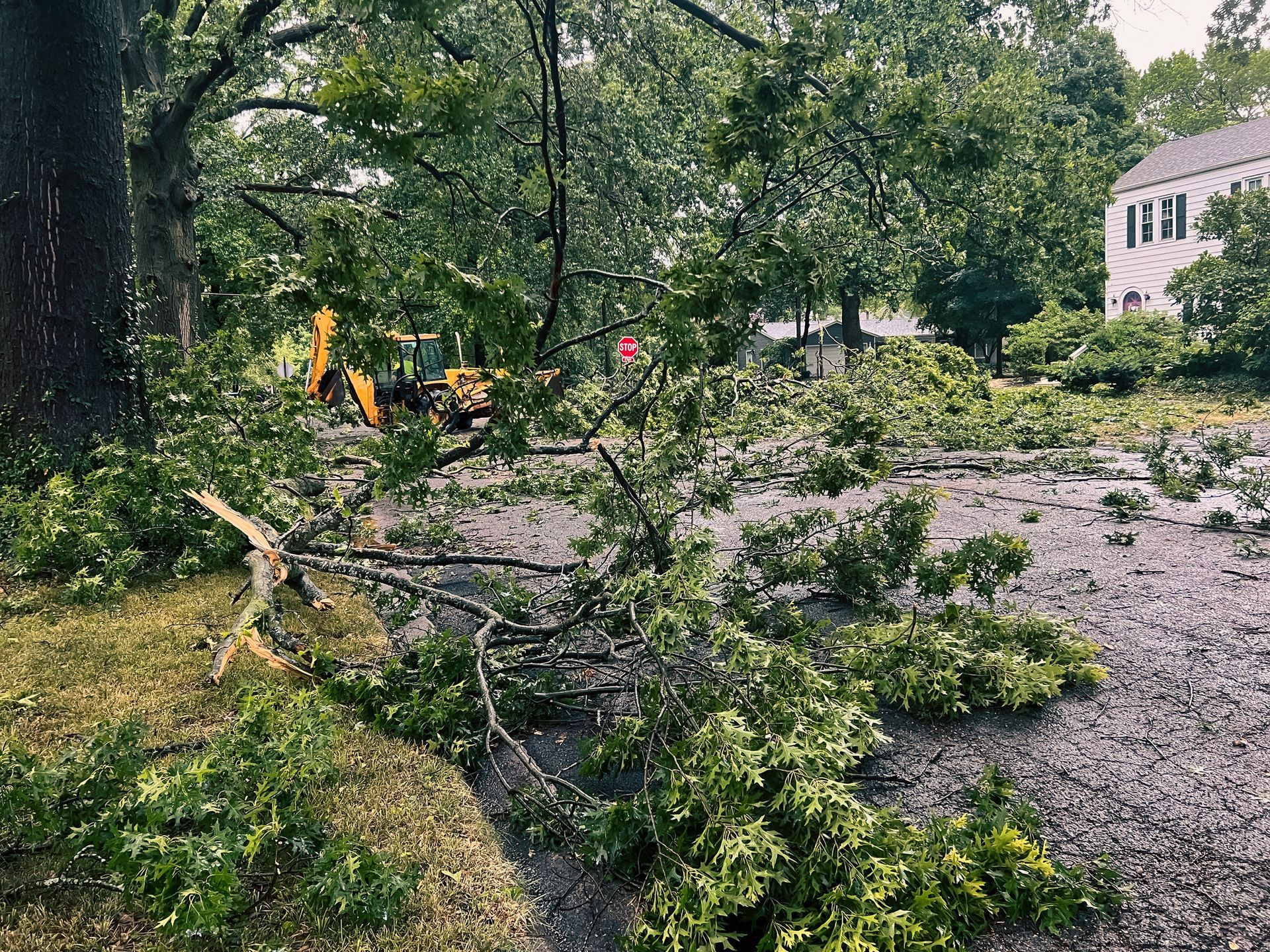 Backhoe clearing debris on residential street after severe residential storm damage and tornado.