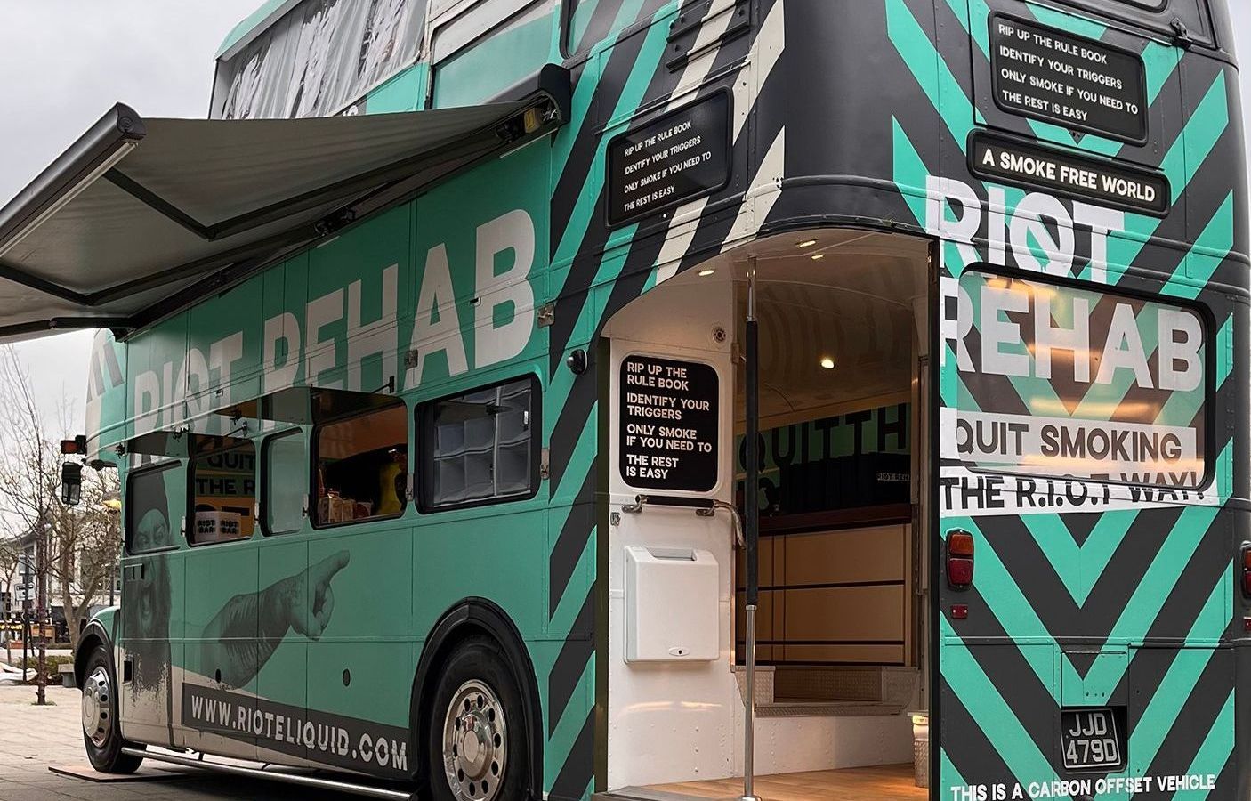 A green and black double decker bus is parked on the side of the road.