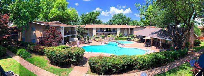 A large swimming pool is surrounded by trees and bushes in front of a house.
