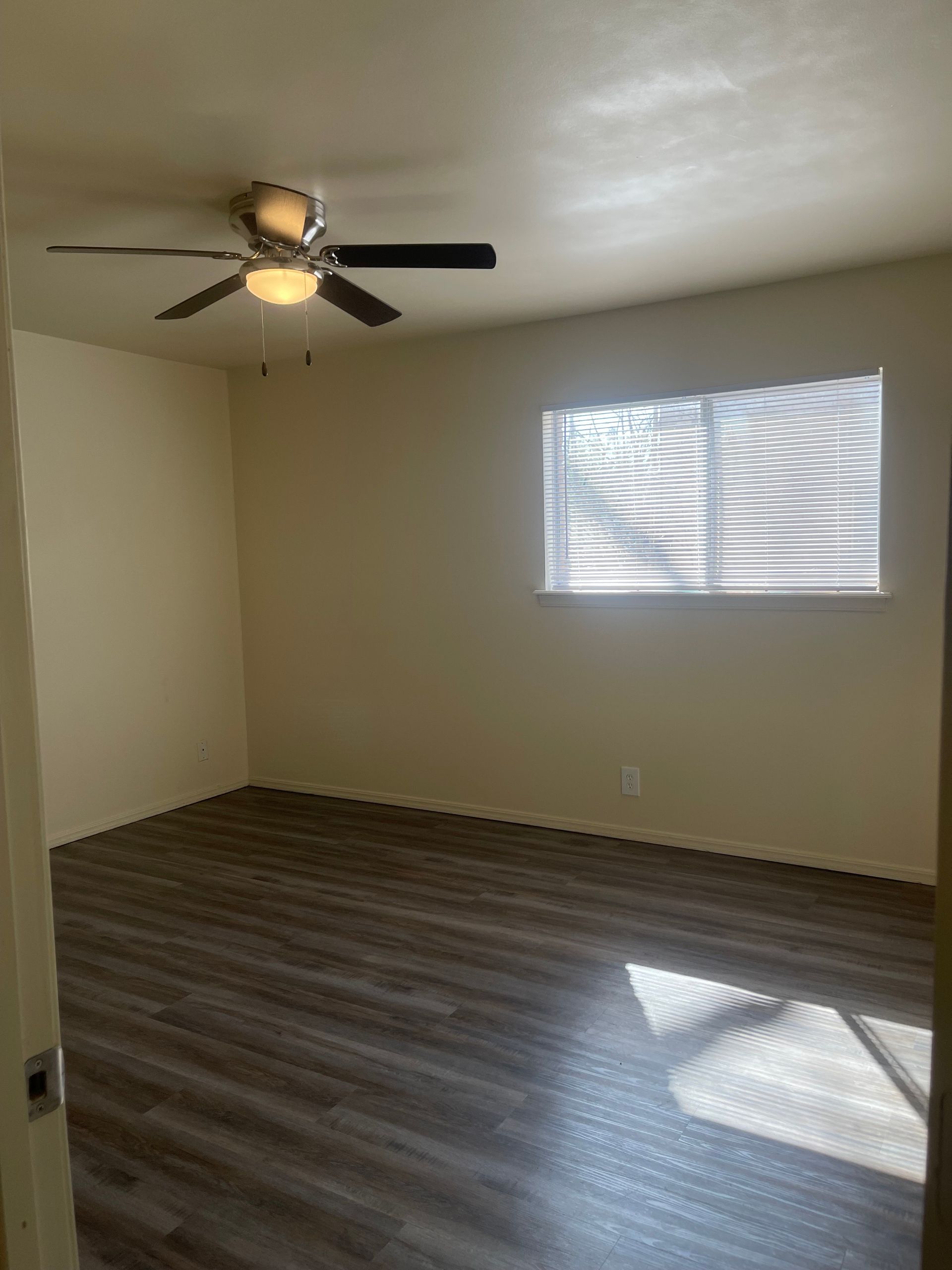 An empty room with a ceiling fan and a window.