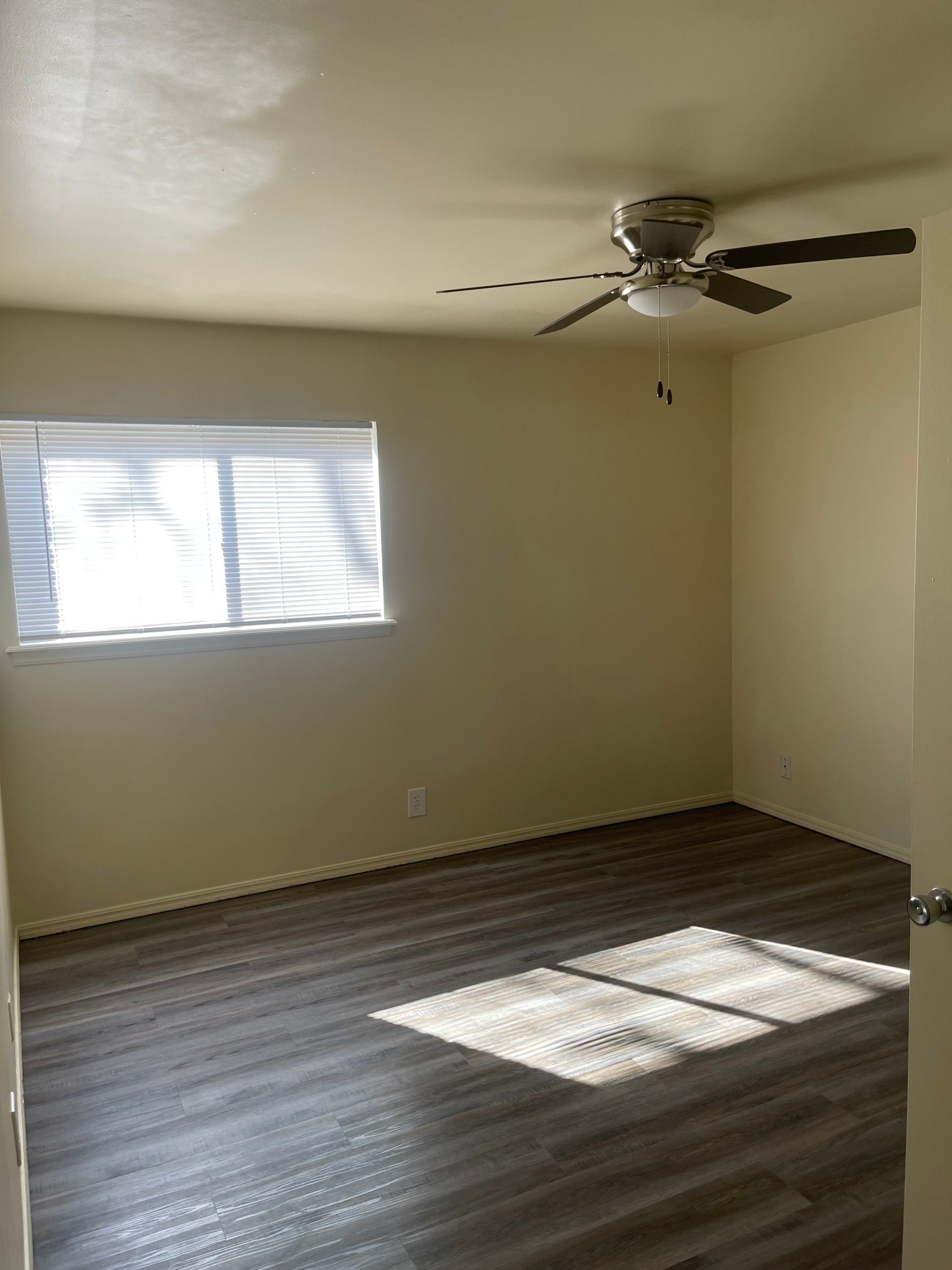 An empty room with a ceiling fan and a window.