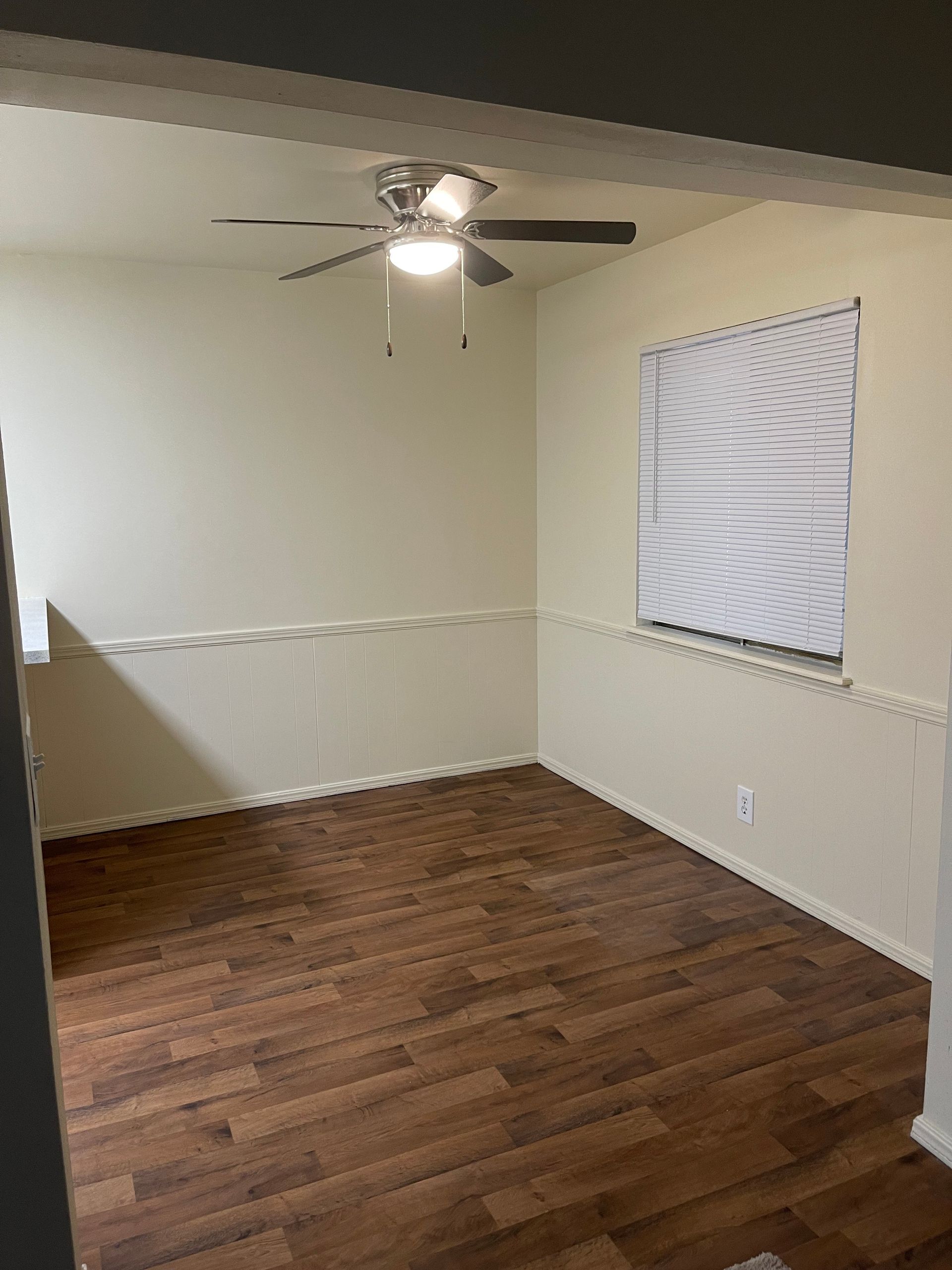 An empty room with hardwood floors and a ceiling fan.