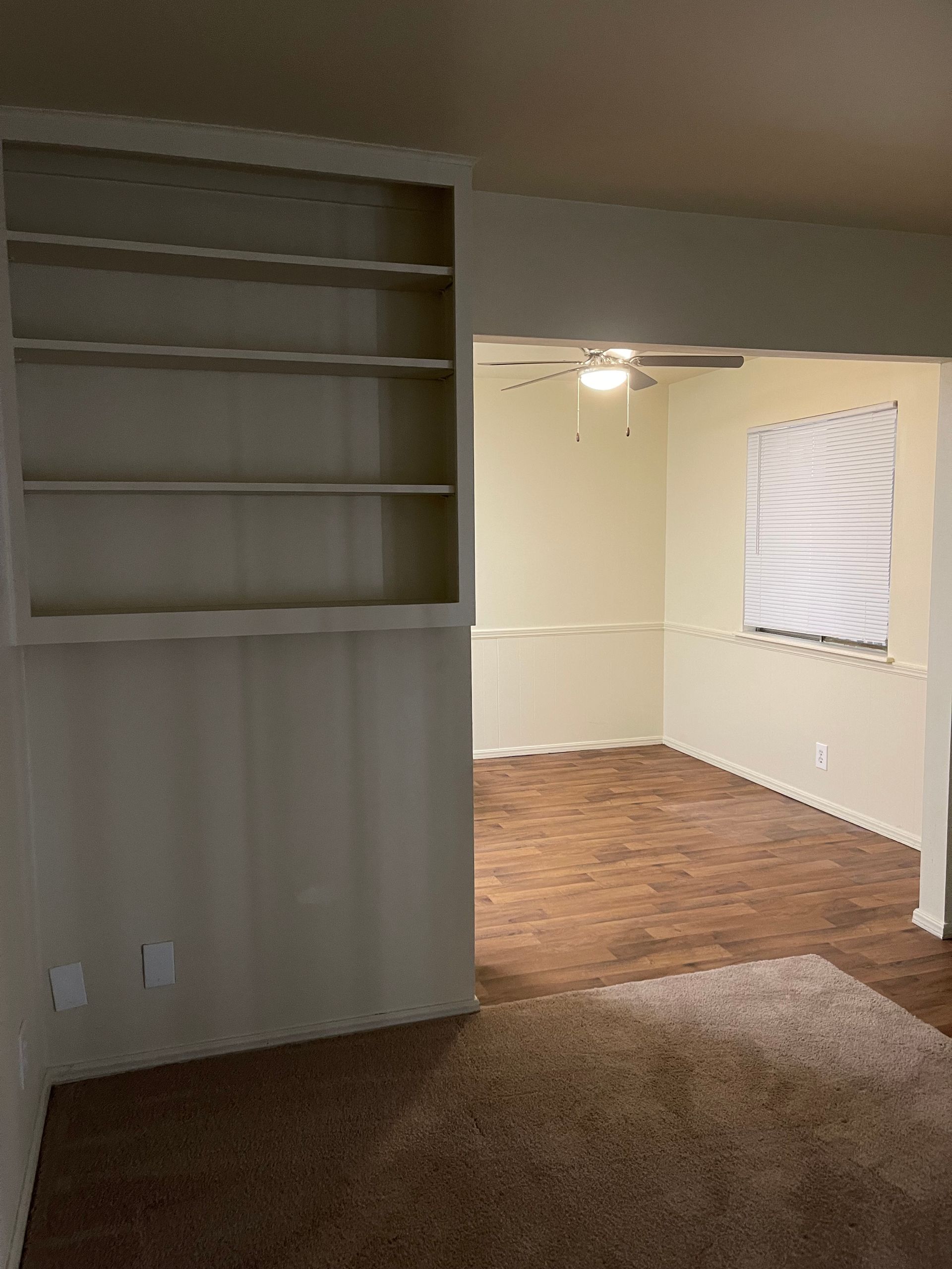 An empty living room with a ceiling fan and a window.