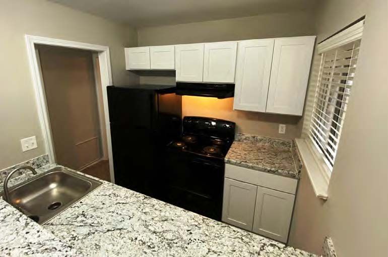 A kitchen with white cabinets , a black stove , a black refrigerator , a sink , and a window.