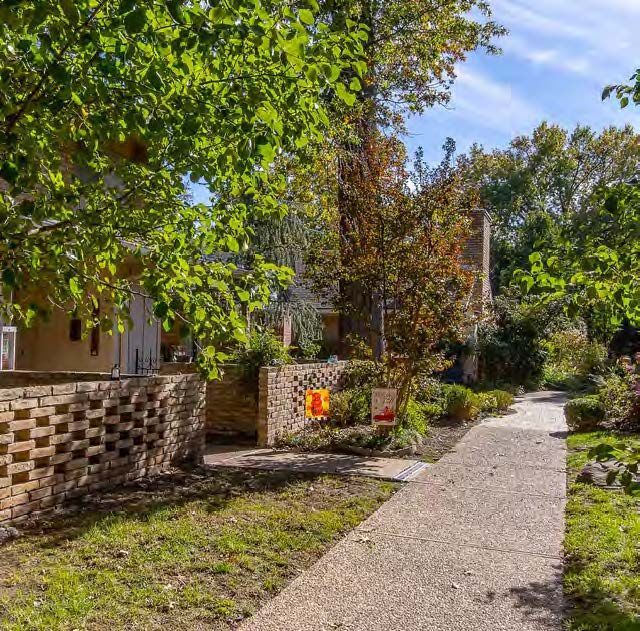 A sidewalk leading to a house surrounded by trees and grass.