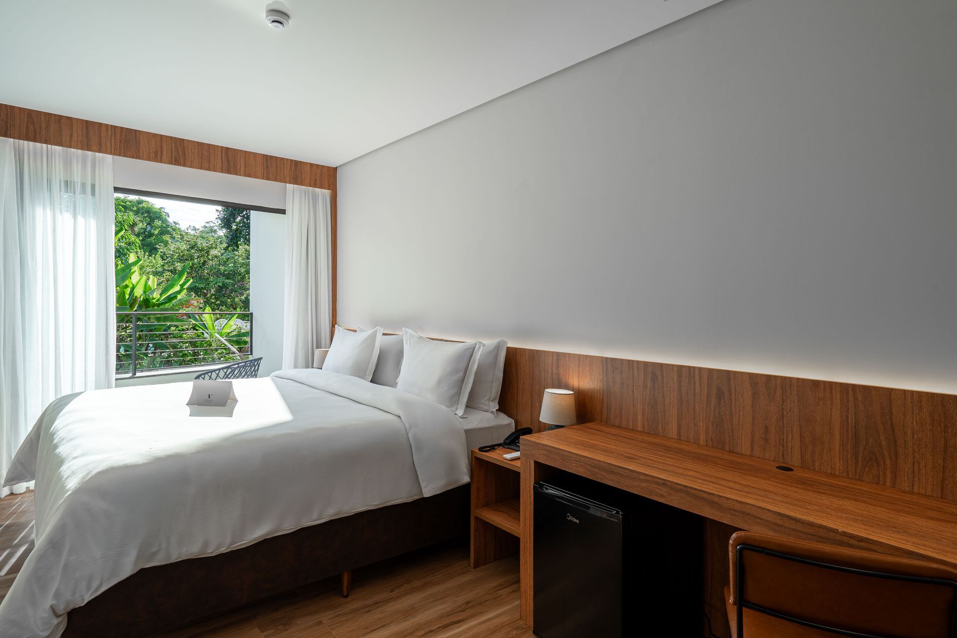 Um quarto de hotel com uma cama, escrivaninha e janela.