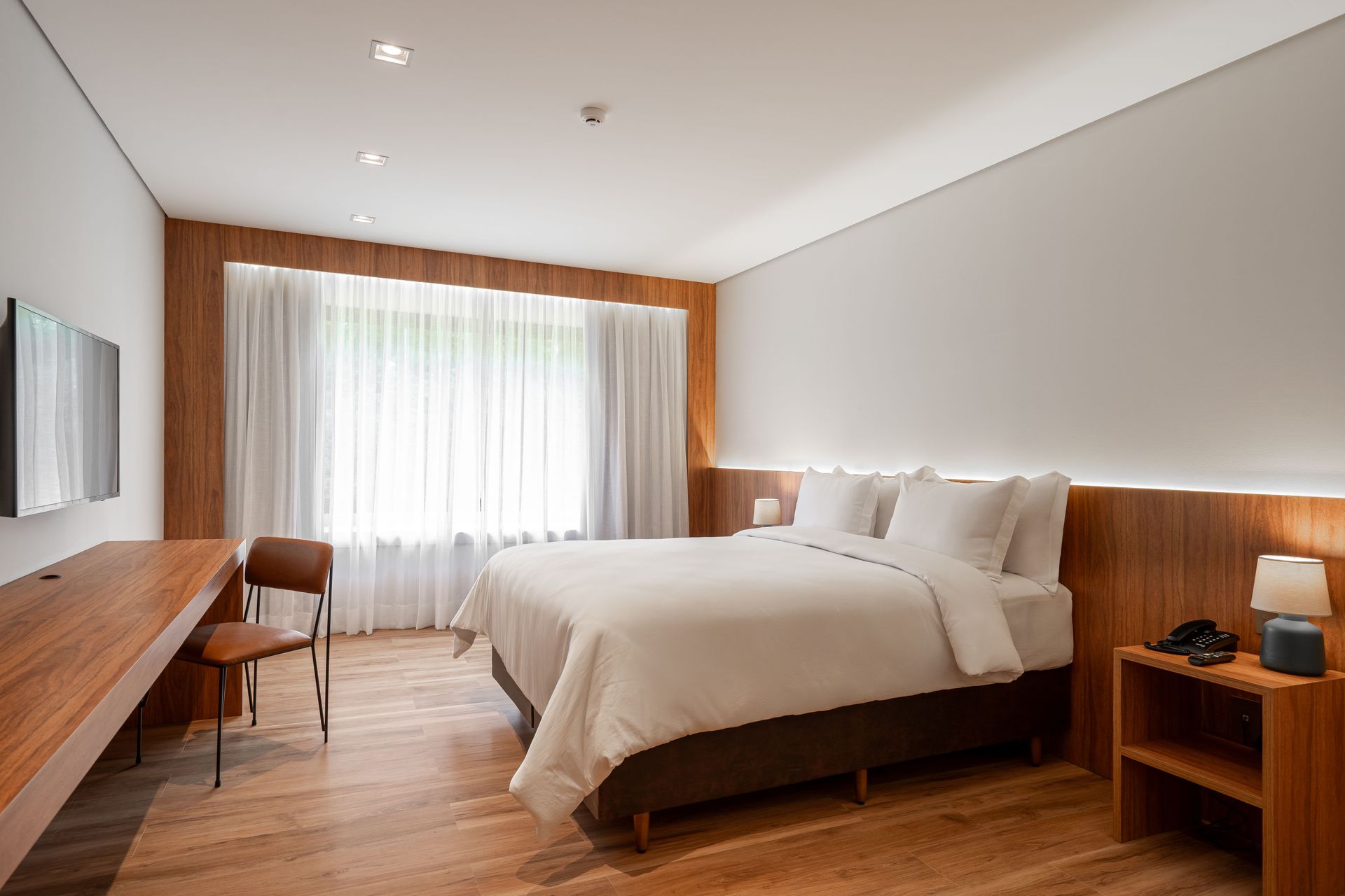 Um quarto de hotel com uma cama, escrivaninha, cadeira e televisão.