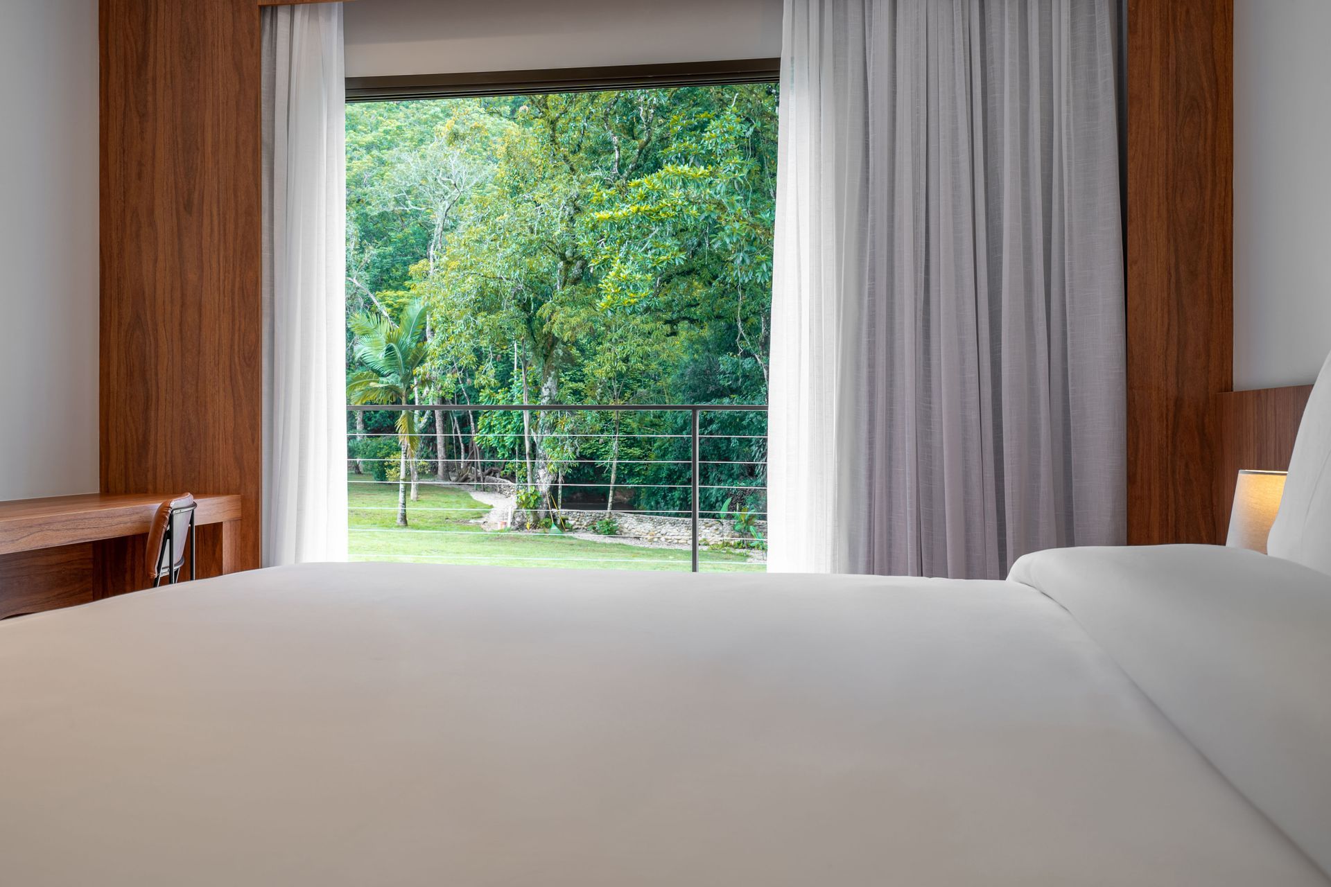 Um quarto de hotel com uma cama e uma grande janela com árvores ao fundo.