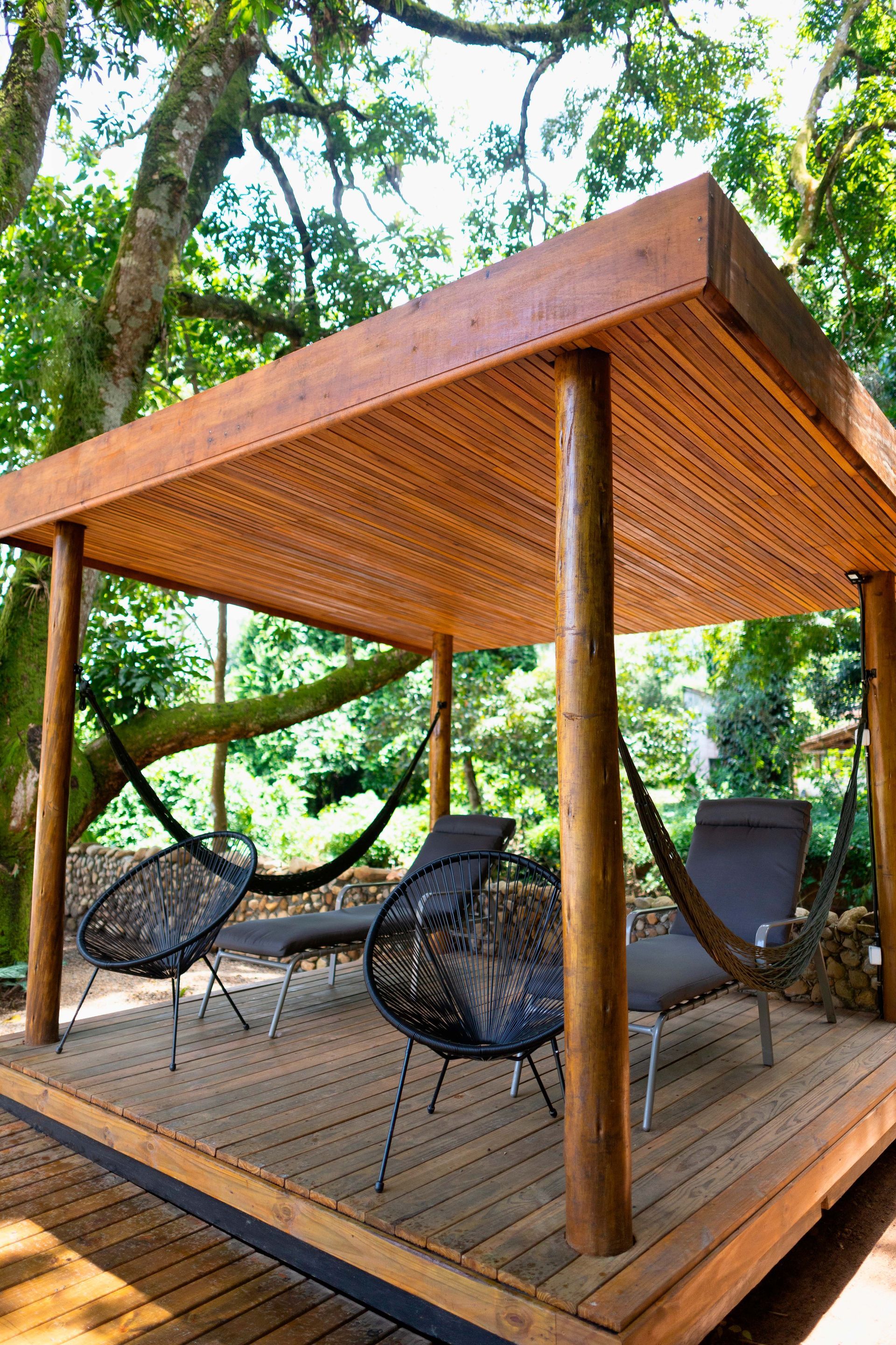 Um gazebo de madeira com cadeiras e redes embaixo.