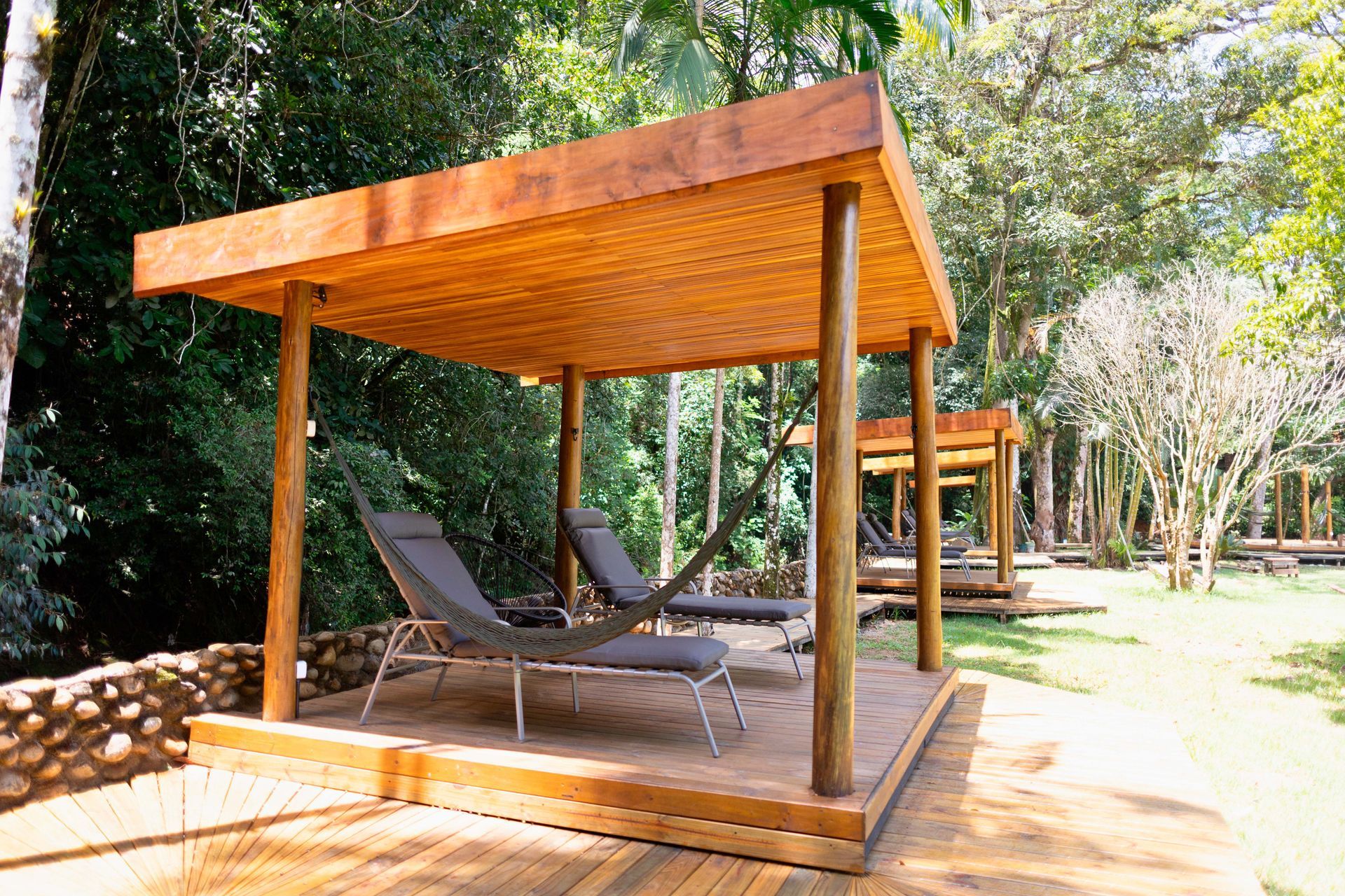 Um gazebo de madeira com cadeiras embaixo no meio de uma floresta.