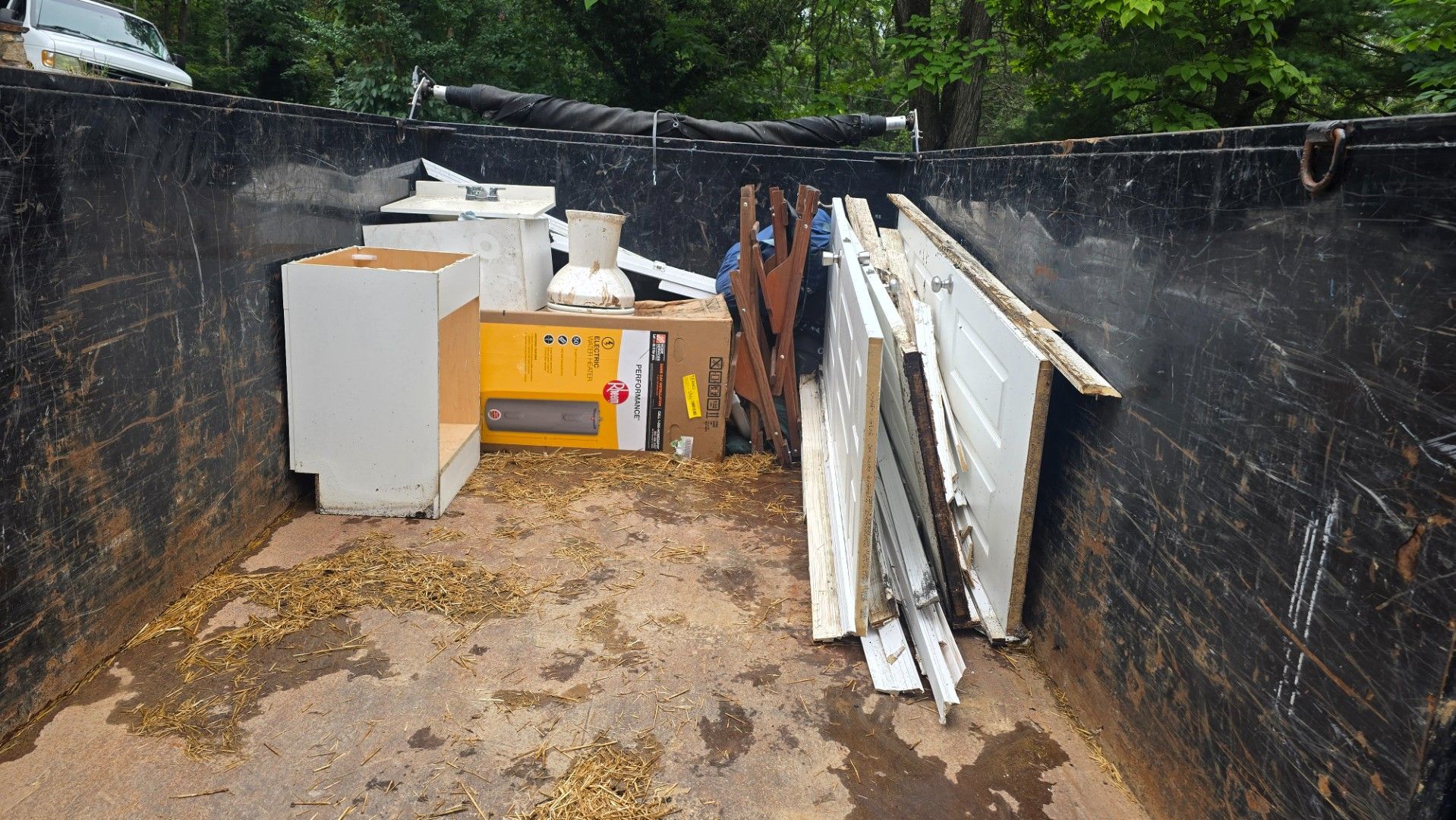 A dumpster filled with construction debris: wood, cardboard boxes, and a small appliance.