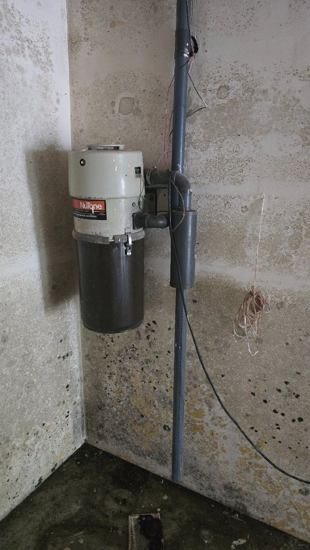 Water pump attached to a pipe on a concrete wall in a basement corner.