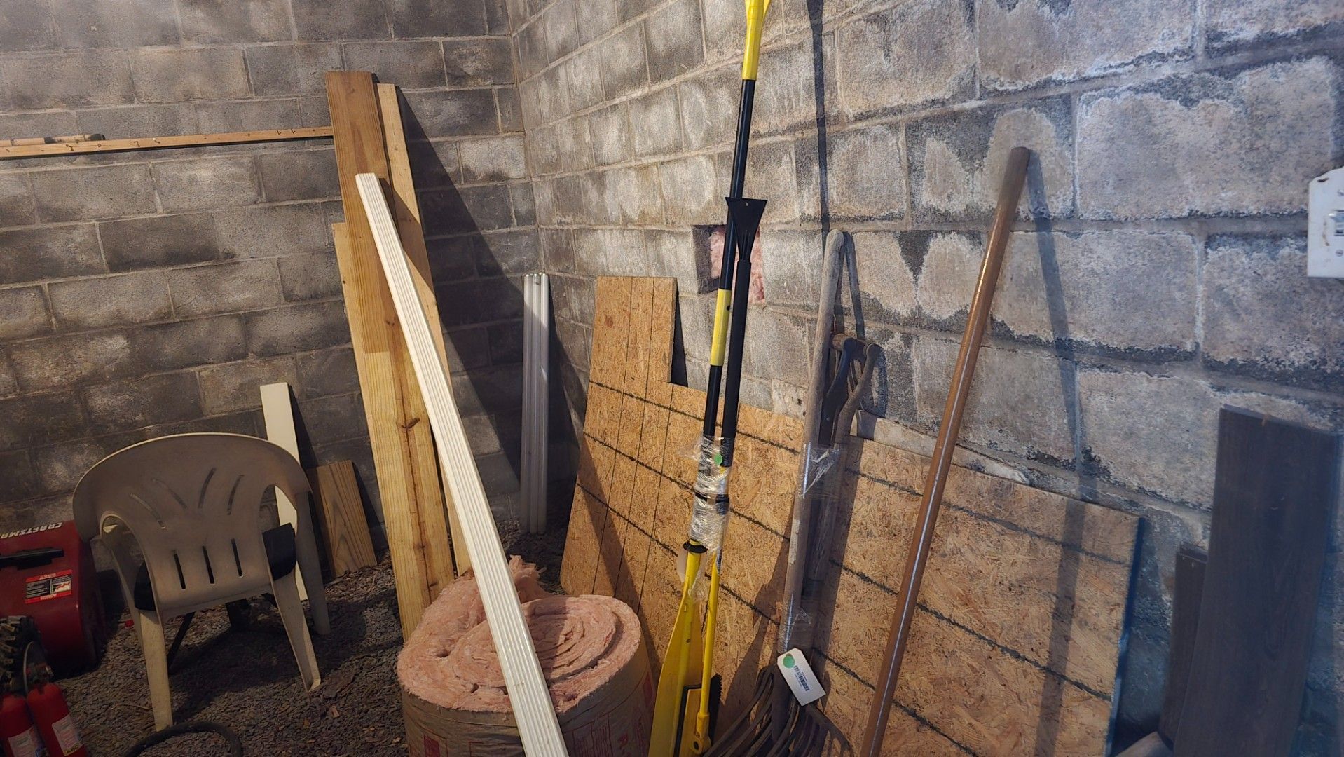 Basement storage area with various tools, wood planks, a chair, and other debris against cinder block walls.