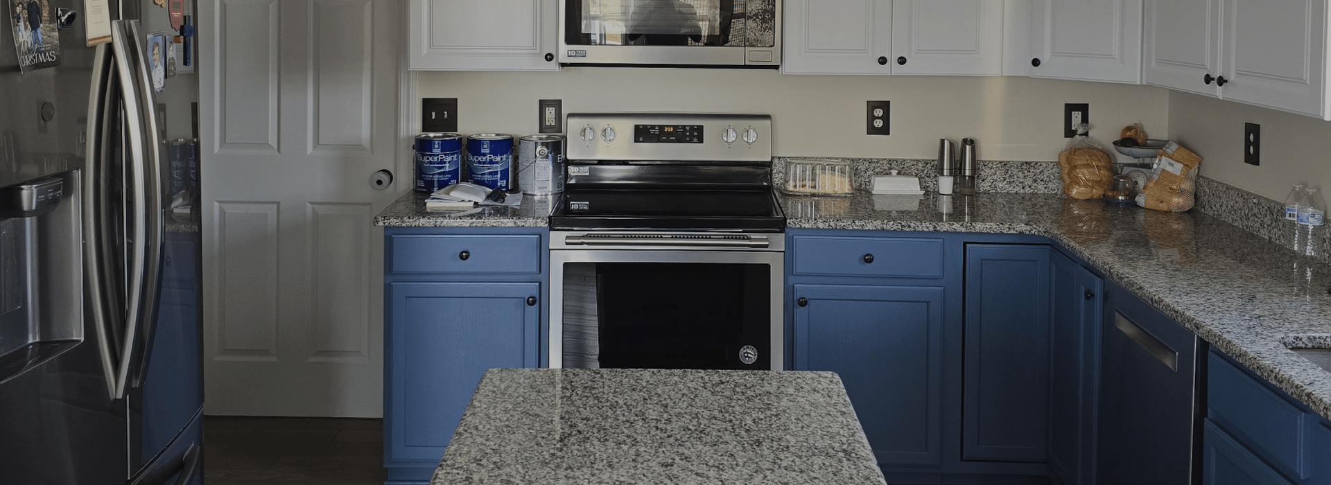 Blue kitchen cabinets with white upper cabinets, granite countertops, and a stainless steel appliance.