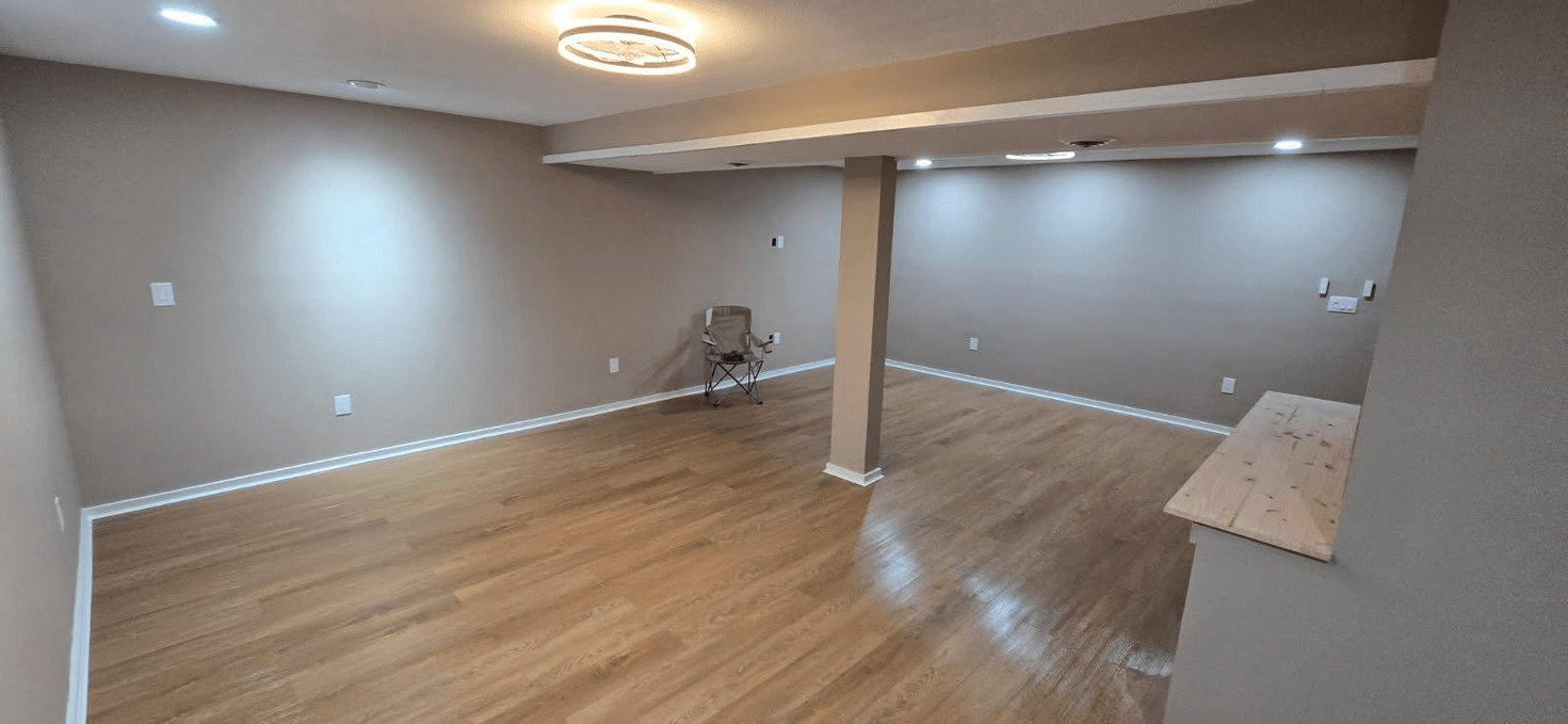 Empty room with hardwood floors and gray walls, lit by recessed lights and a ceiling fixture.