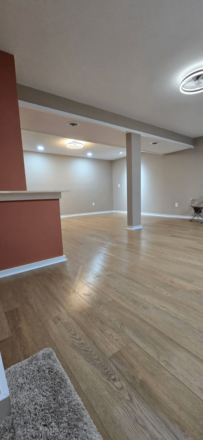 A large, empty room with wood floors, neutral walls, and recessed lighting. A red wall is visible.