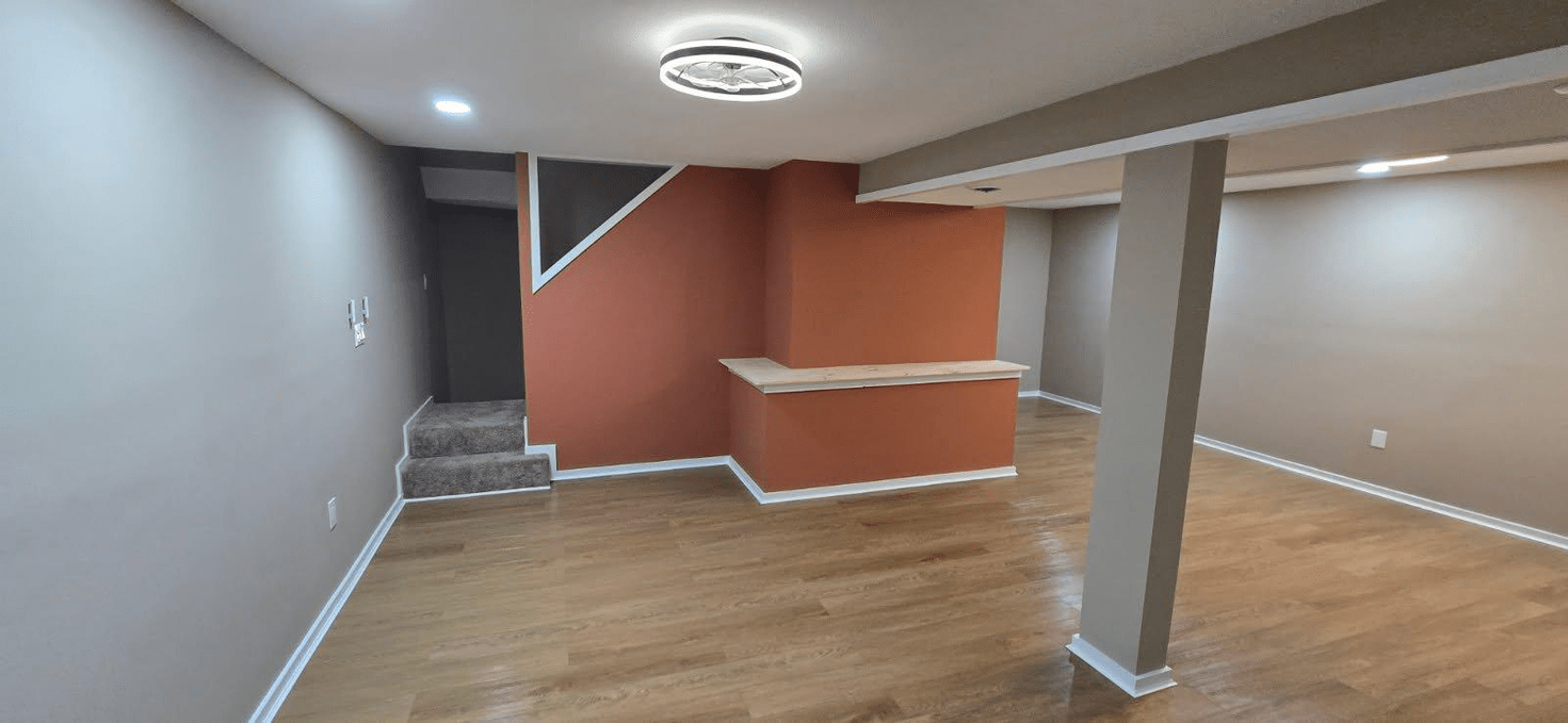Basement with orange accent wall, stairs, and light wood floors.
