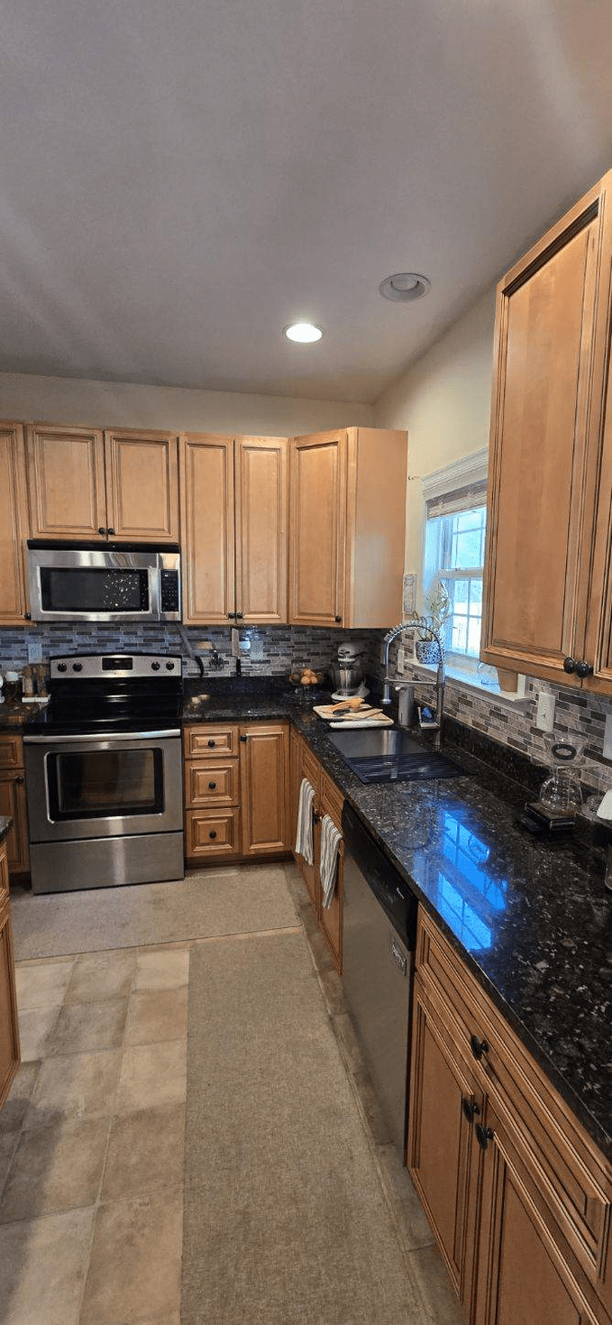 Kitchen with light-colored cabinets, stainless steel appliances, dark countertops, and a window.