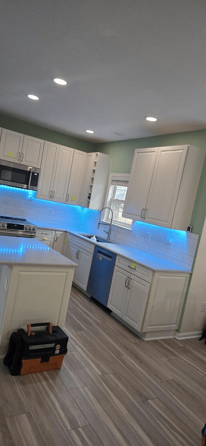 A newly renovated kitchen with white cabinets, blue under-cabinet lights, and a toolbox on the floor.