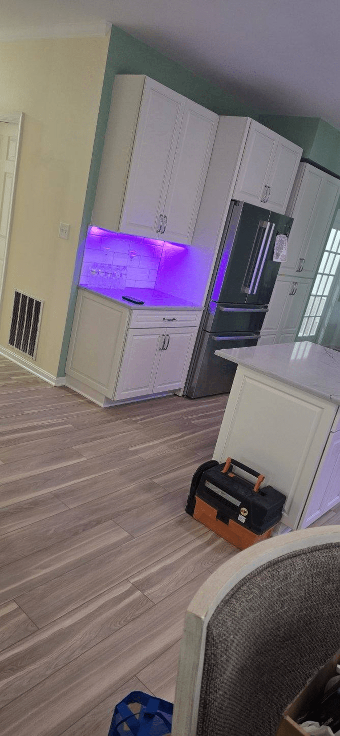 Kitchen with white cabinets, purple under-cabinet lighting, and a toolbox on the floor.