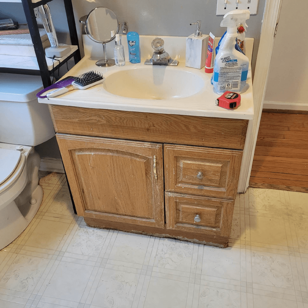 Bathroom vanity with a white sink, wooden cabinets, and various toiletries on the counter.