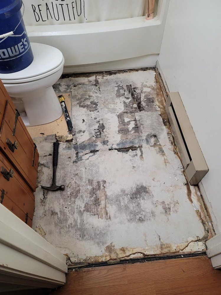 Bathroom floor with damaged subfloor exposed, toilet, and tools.