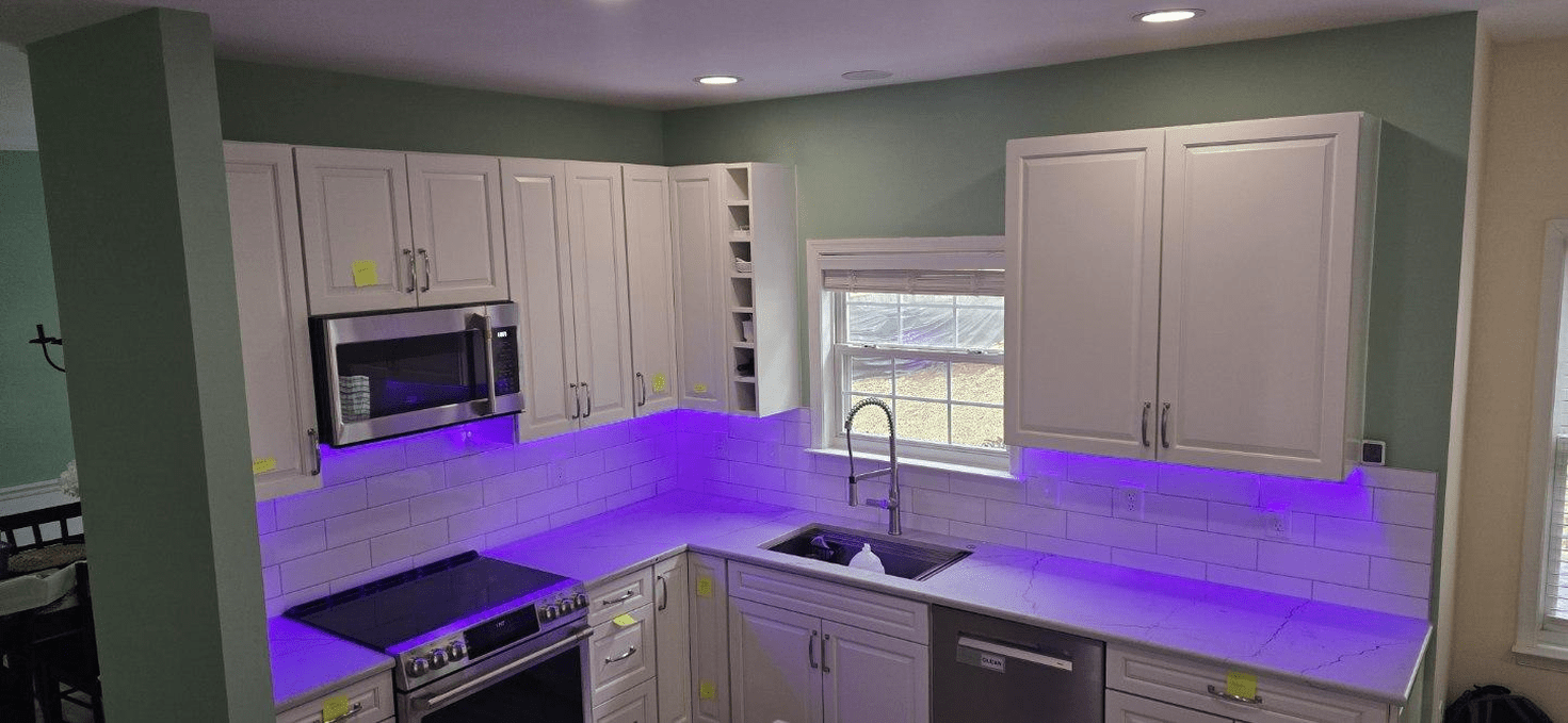 A kitchen with white cabinets, purple under-cabinet lighting, and a green wall.