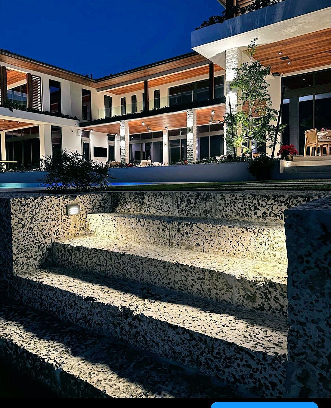 Modern luxury villa at dusk with illuminated stone steps leading to a poolside patio.