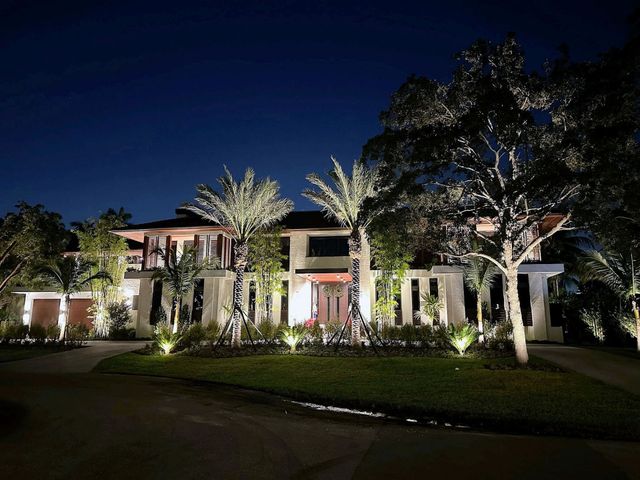 Illuminated two-story house at night with palm trees and a landscaped front yard