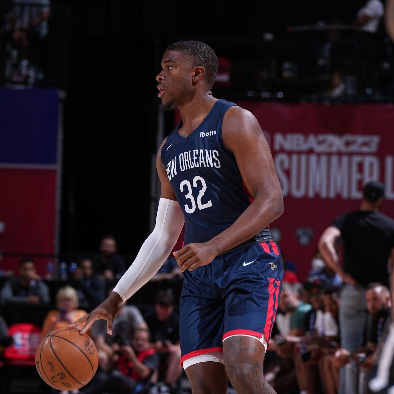Basketball player dribbling ball, wearing New Orleans Pelicans jersey, in a Summer League game.