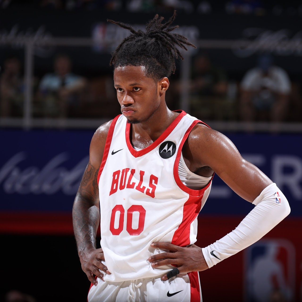 Basketball player in a Chicago Bulls jersey with dreadlocks, hands on hips, looking down. Court setting.