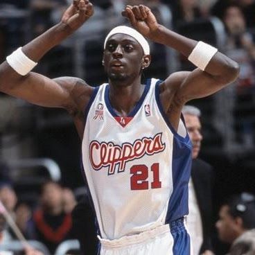 Basketball player in Clippers jersey with arms raised, white headband and wristbands.