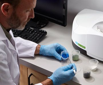 A man in a lab coat and blue gloves is working on a computer. rothgreaves ptfe coatings