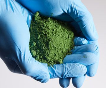 A person wearing blue gloves is holding a pile of green powder rothgreaves ptfe coatings