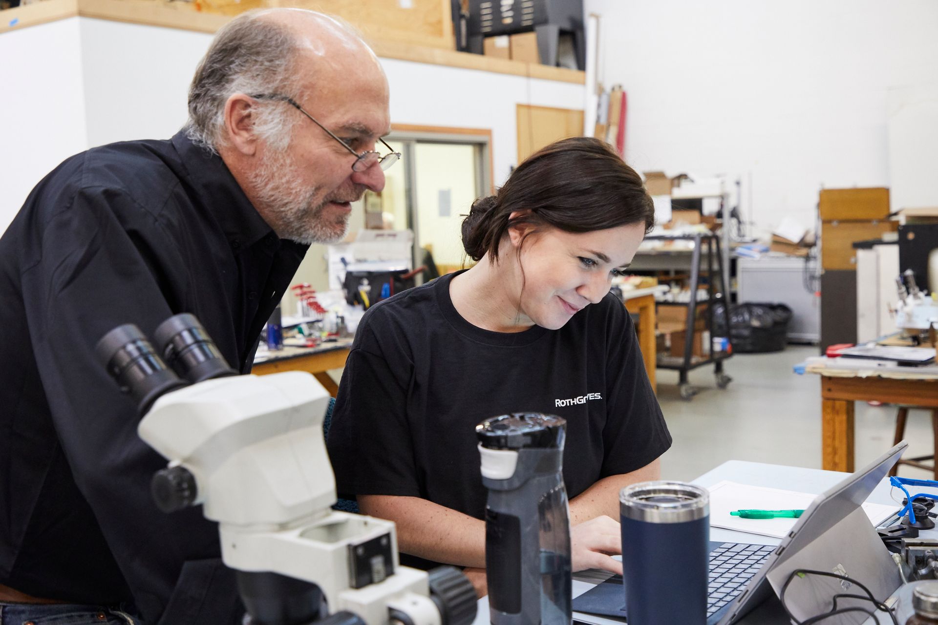 A man and a woman are looking through a microscope at a laptop. rothgreaves coil winders and ptfe coatings