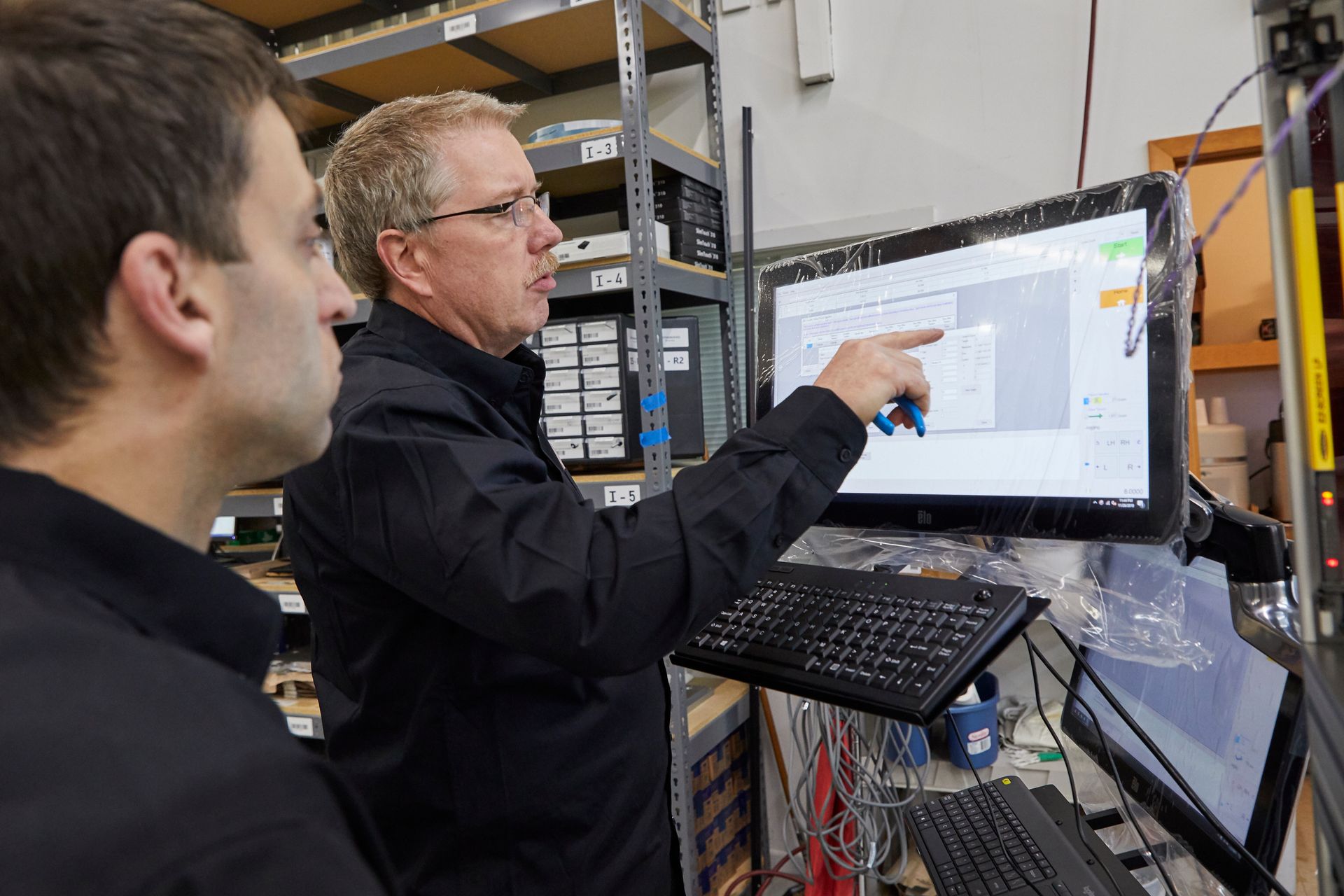 Two men are looking at a computer screen in a warehouse.