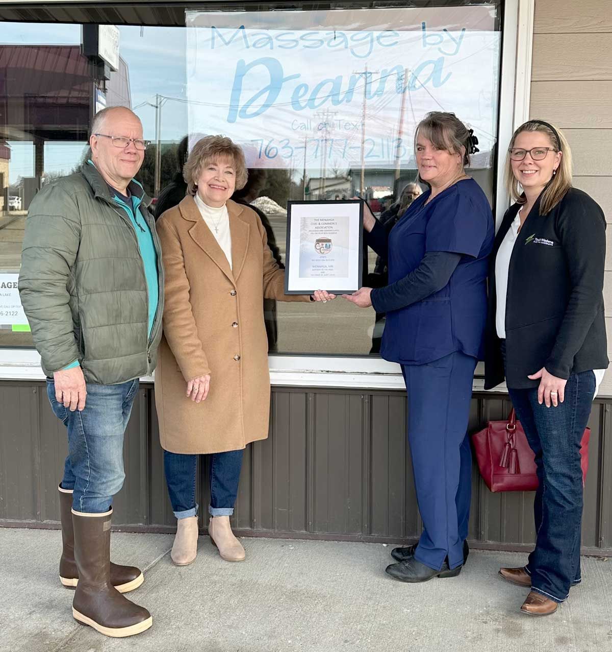 Four people stand in front of a Massage by Deanna storefront holding a framed certificate.
