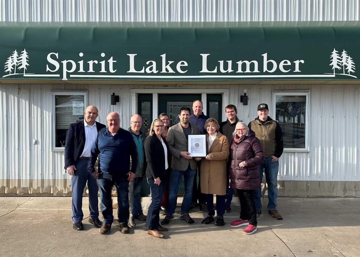 A group of people standing outside Spirit Lake Lumber, one person holding a framed award.
