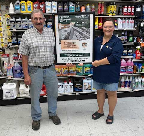 Two people stand in an auto parts store holding a framed raffle poster for a chance to win a car.