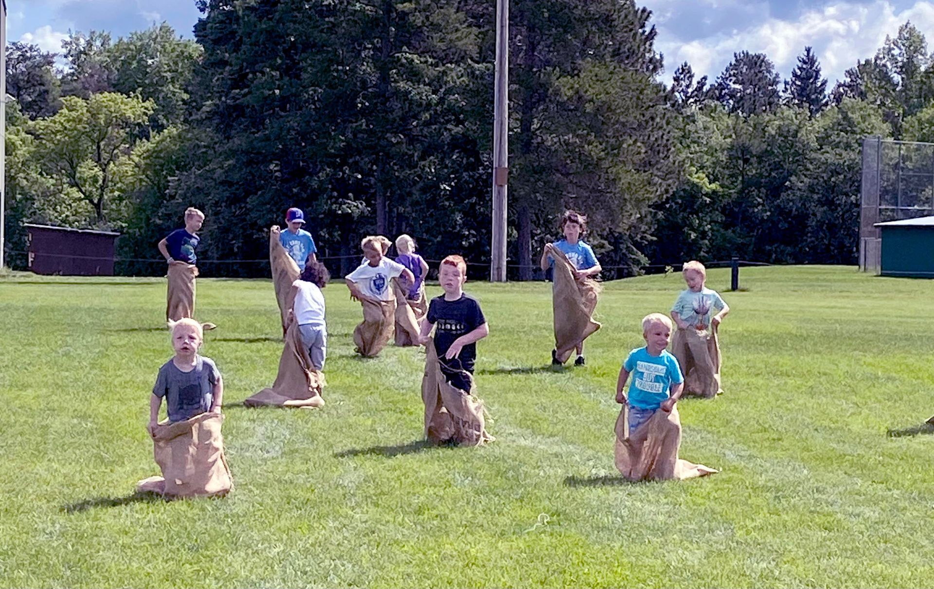 A group of children participating in a burlap sack race on a grassy field during a sunny day.