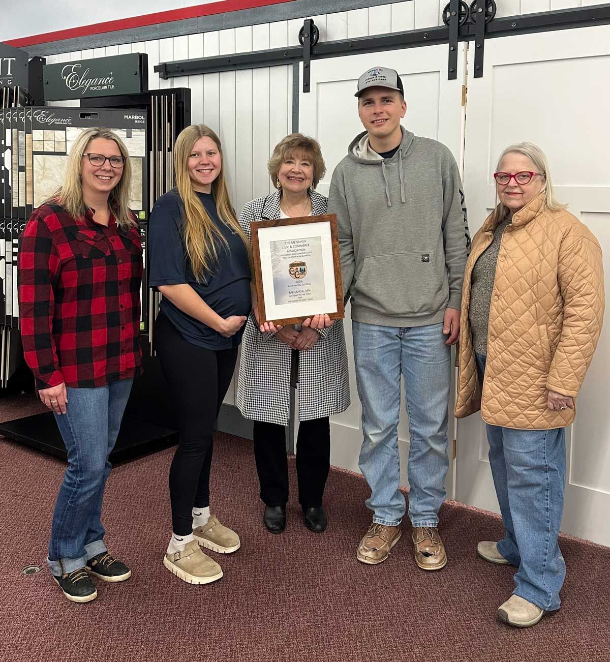 Five people stand in a showroom, the center person holding a frame, smiling toward the camera.